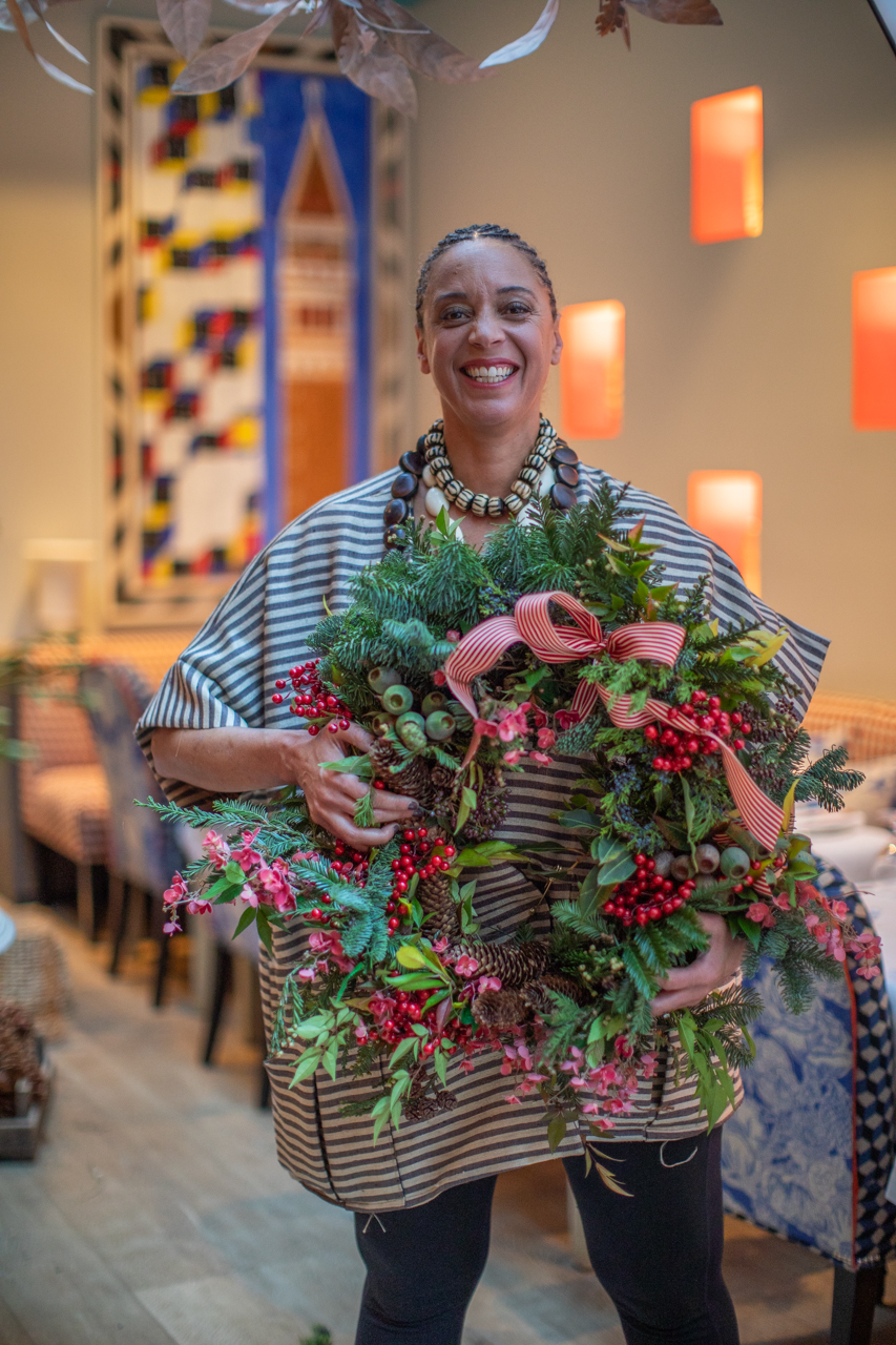 A portrait of florist Tawana Schlegel holding a wreath in the Orangery at Warren Street Hotel