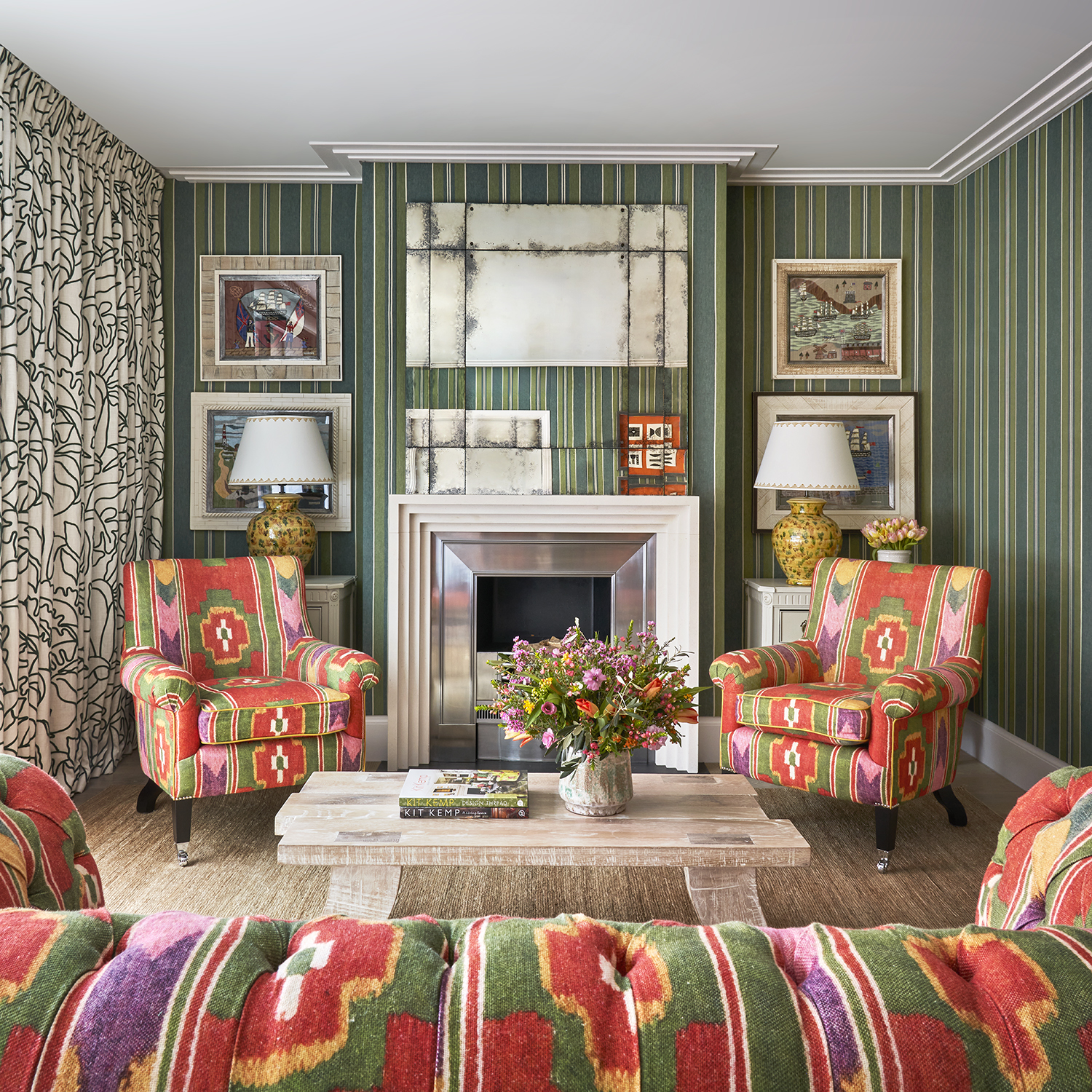 Living room shot of Residence 09, a Luxury Two Bedroom Residence at Ham Yard Hotel. A portrait mage from the back of the sofa, in a bold green and orange print, looking towards armchairs the face the viewer in the same print. A coffee table topped with books and flowers sit in the centre.