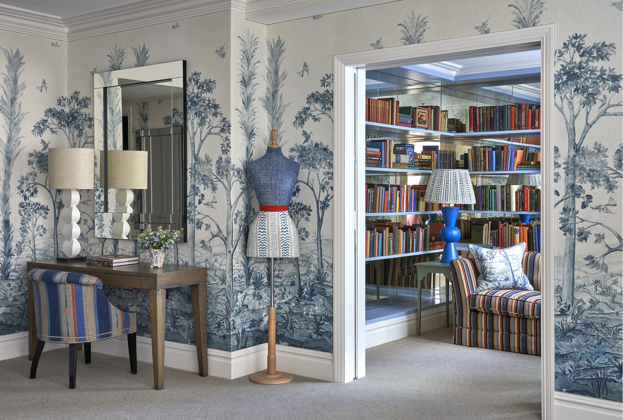 A diagonal shot looking into the alcove section of a Deluxe Junior Snug Suite at Ham Yard Hotel. Next to a writing desk and mannequin, double sliding doors open up to reveal a sofa and bookshelves
