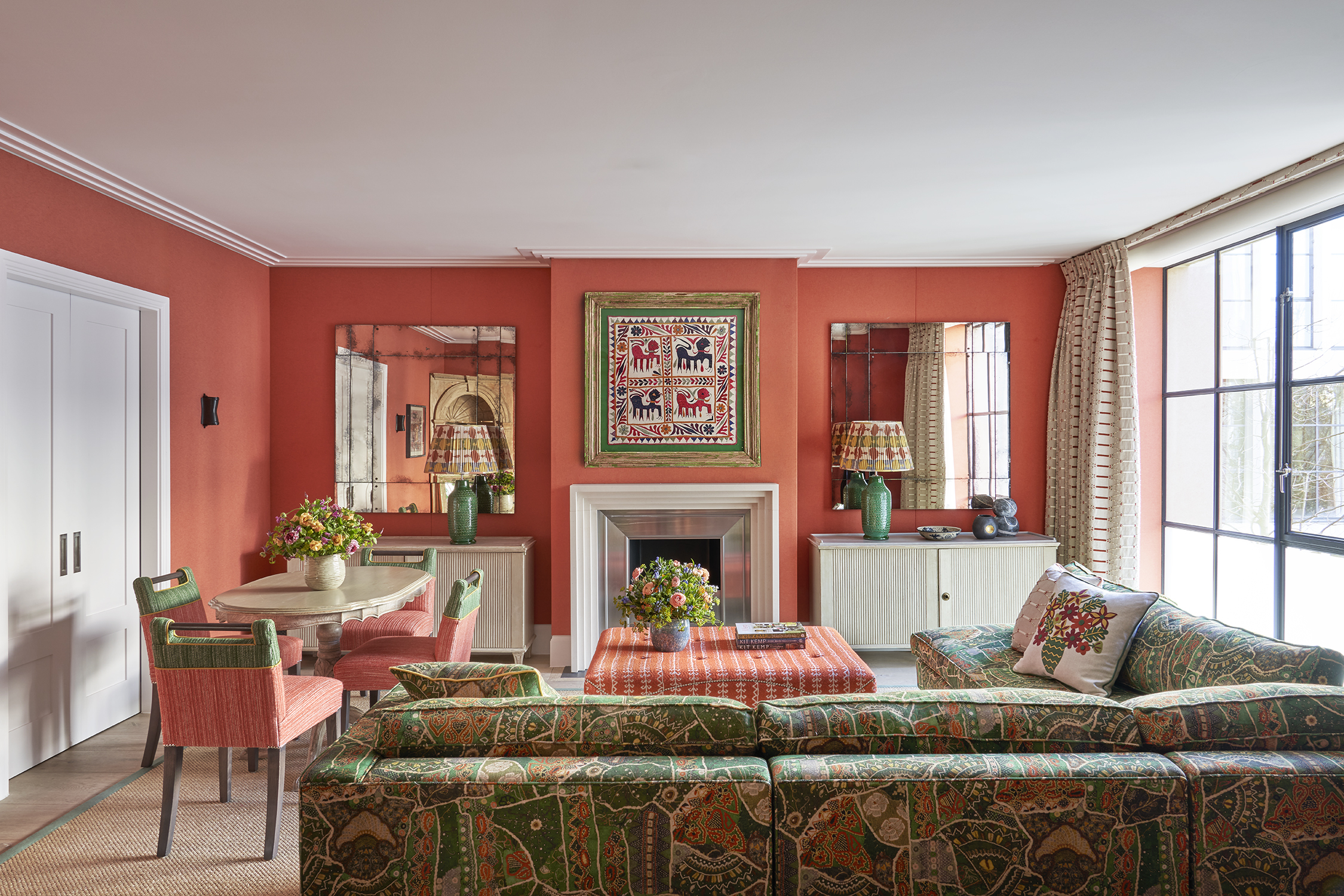 A wide shot of the living area of the Deluxe Two Bedroom Suite Room 5 at Ham Yard Hotel. The image shows the back of a 'L shaped' sofa on the right hand side, pointing towards the fire place. On the left the dining table with 4 chairs around