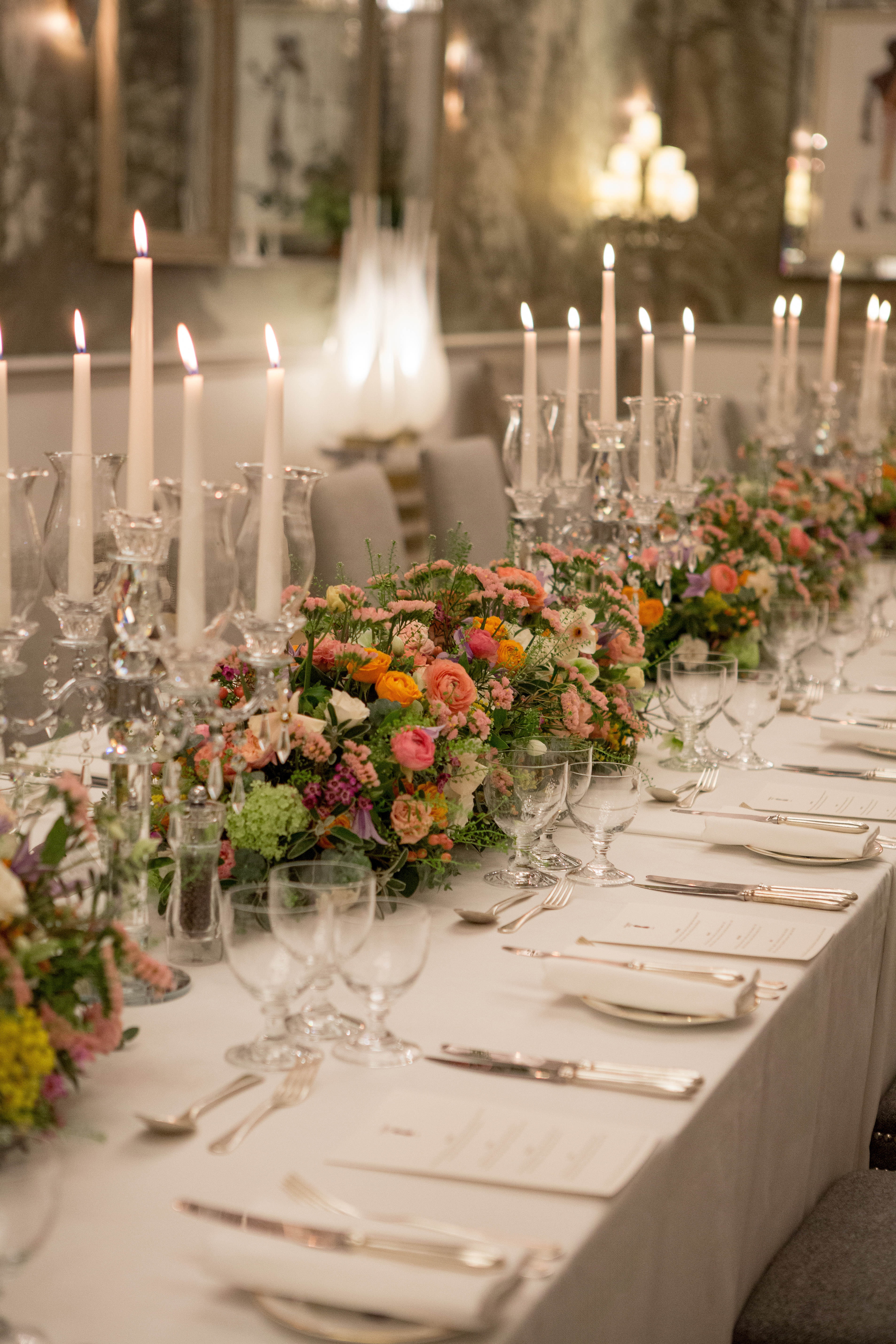 Close up portrait shot of a long dining table dressed with colourful flowers and tall candlesticks in the Shooting Gallery private events room at Haymarket Hotel