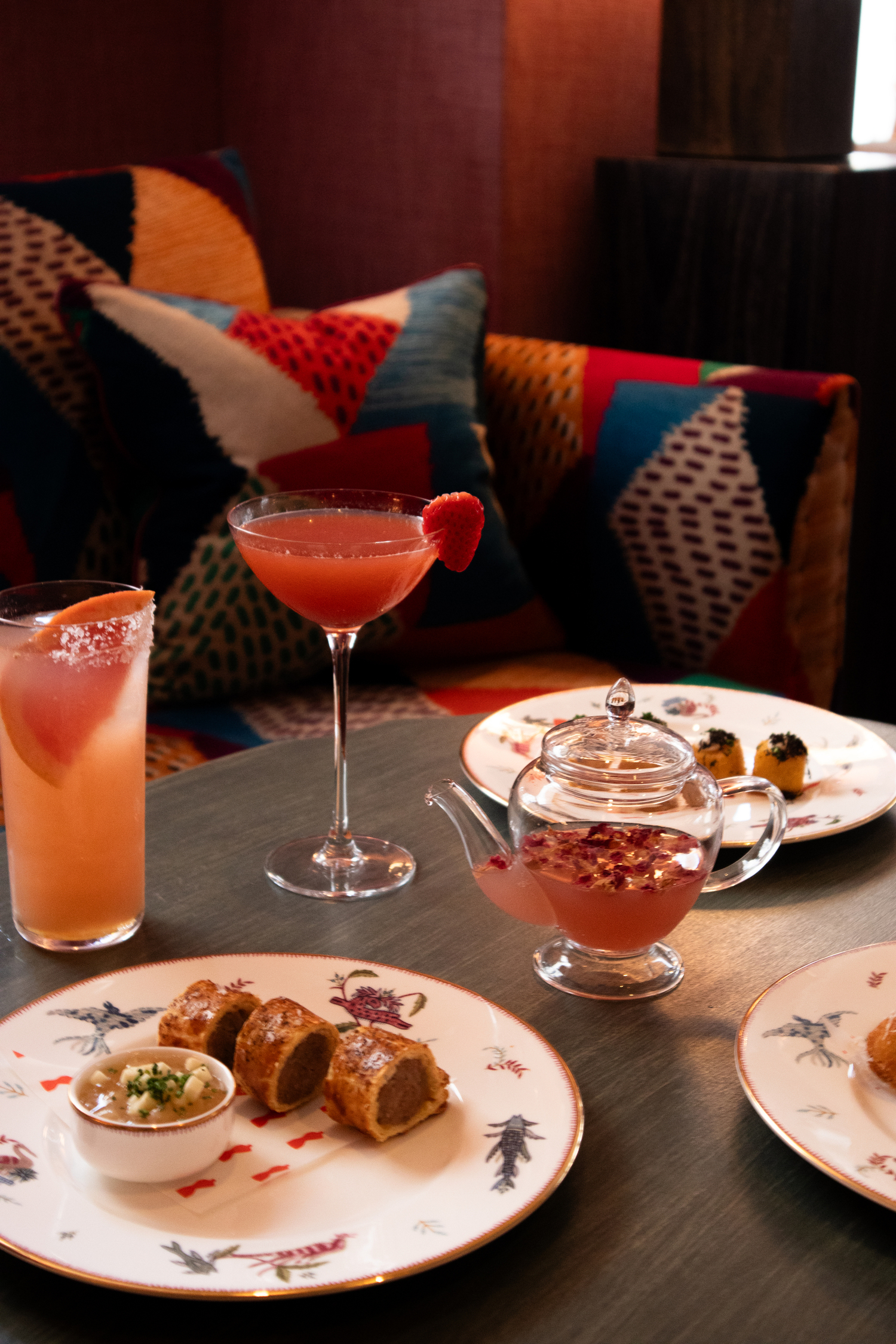 Three pink coloured cocktail and plates of bar snacks at Haymarket Hotel