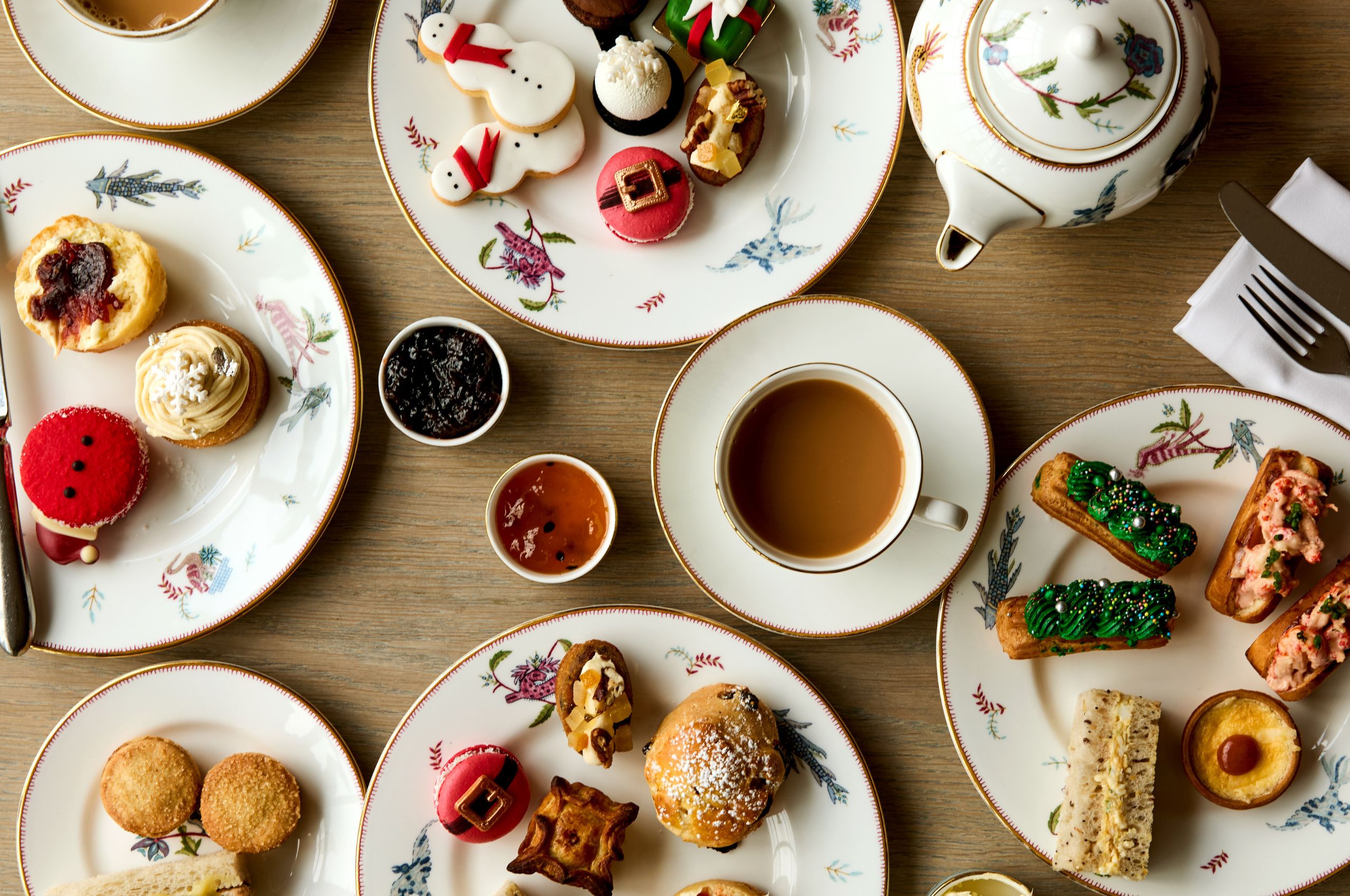 Festive Afternoon Tea shot from above. Cups of tea and plates of cakes and sandwiches laid on a table on Mythical Creatures crockery