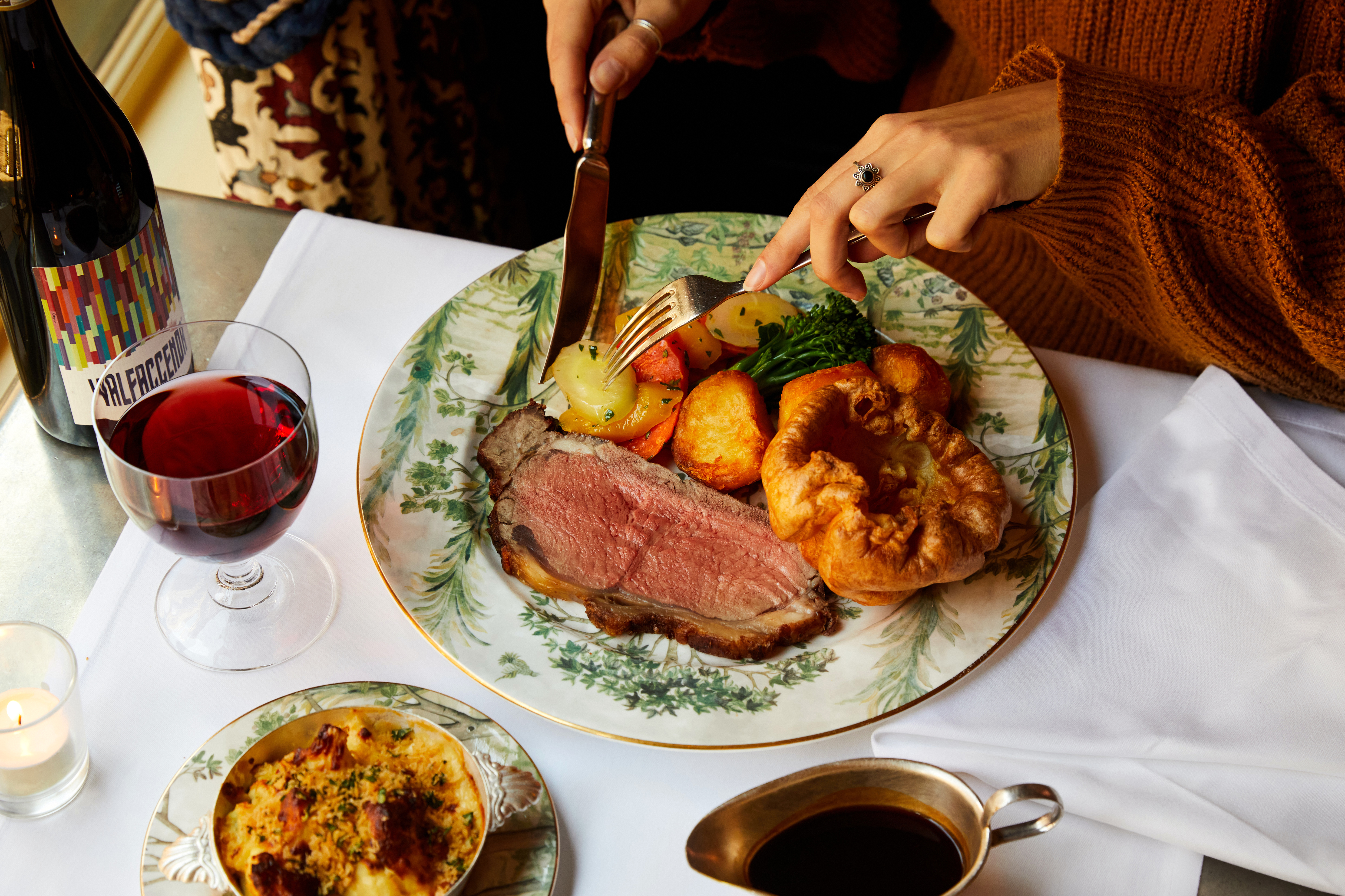Roast beef with Yorkshire pudding and potatoes on a plate at Brasserie Max. Two hands cut into the meal