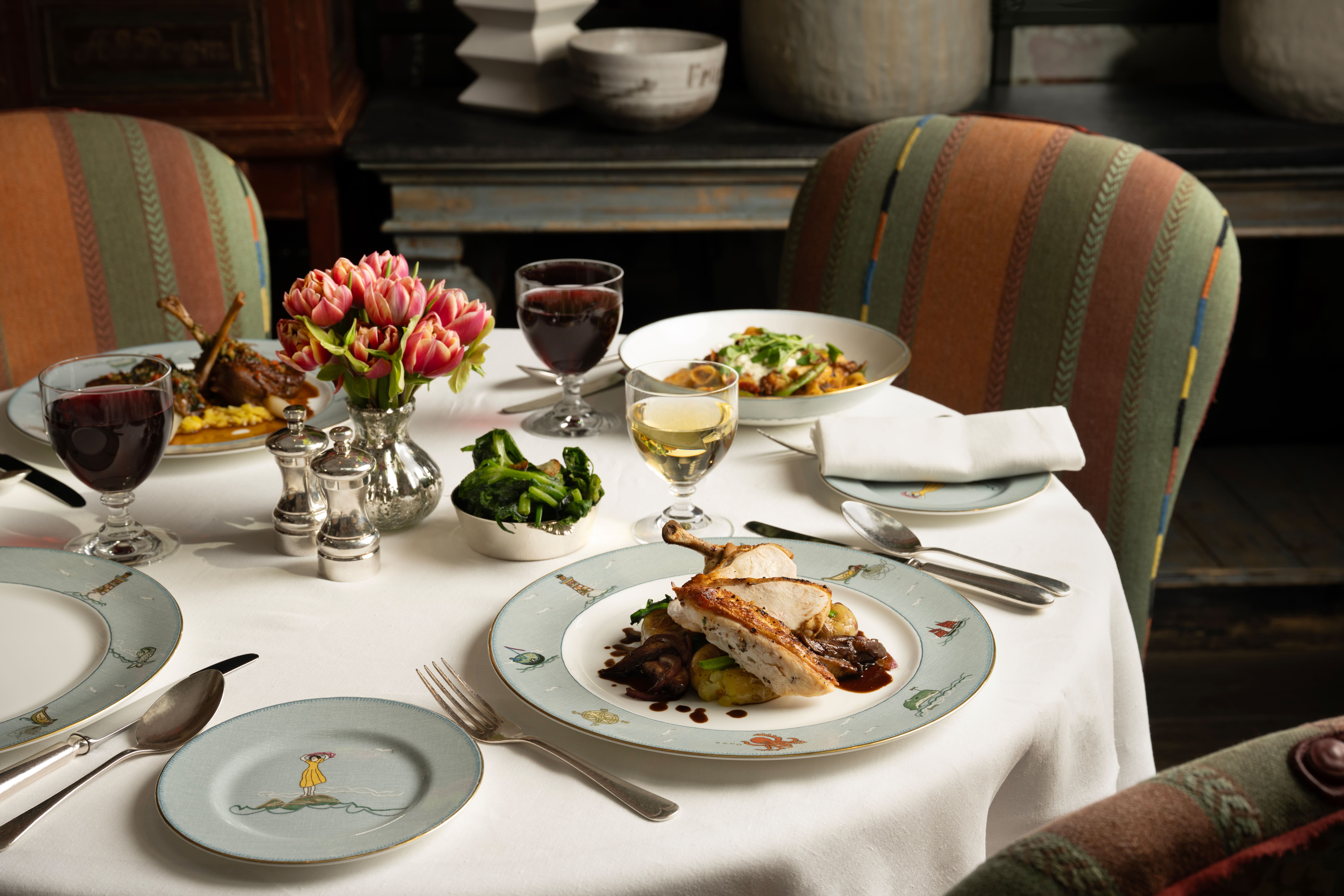 A wide close up shot of a table set up for dinner in The Whitby Bar. There are plates of Lancaster chicken and lamb rigatoni, with wine pairings.