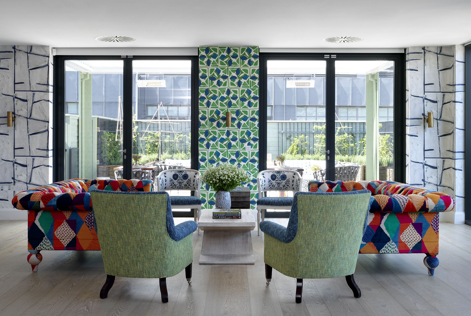 A wide shot of the view of the entertaining area on the top floor Buildings featuring a lounge seating area and floor-to-ceiling windows and doors with views onto the Roof Terrace at 9-11 Richmond Buildings