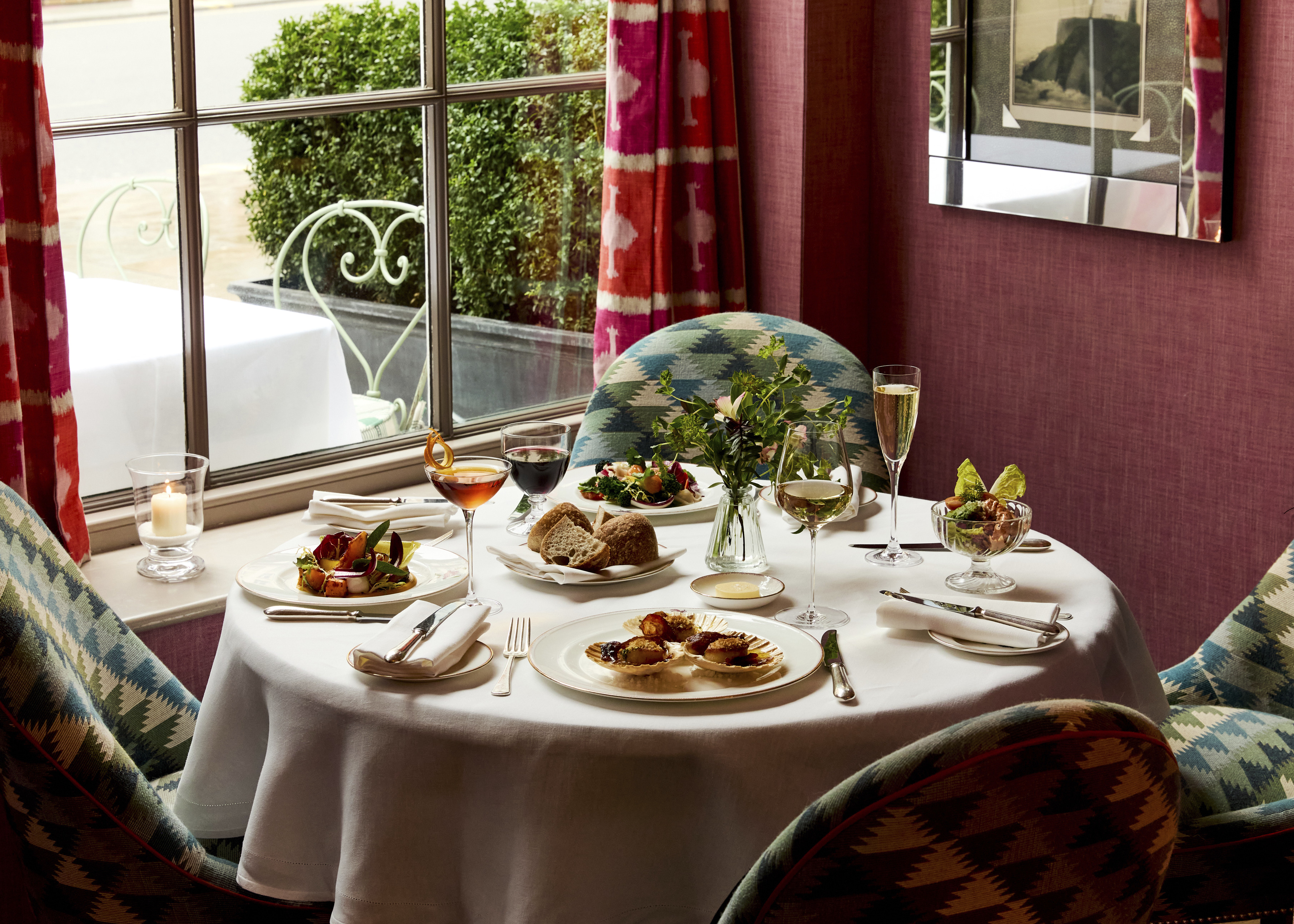 A table in front of a window at Brumus laid with four appetisers accompanied by glasses of wine and cocktails