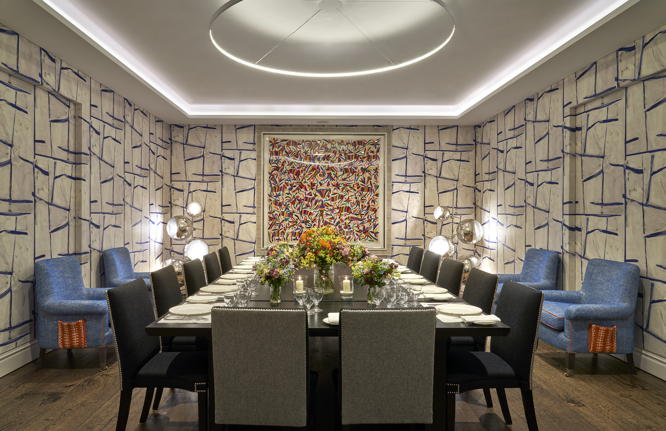 An image of the long dining table set up with flowers, place mats, plates, cutlery and glassware ready for dining in the Sandra Blow, private events room, at The Soho Hotel. With 14 grey chairs around the long tables.