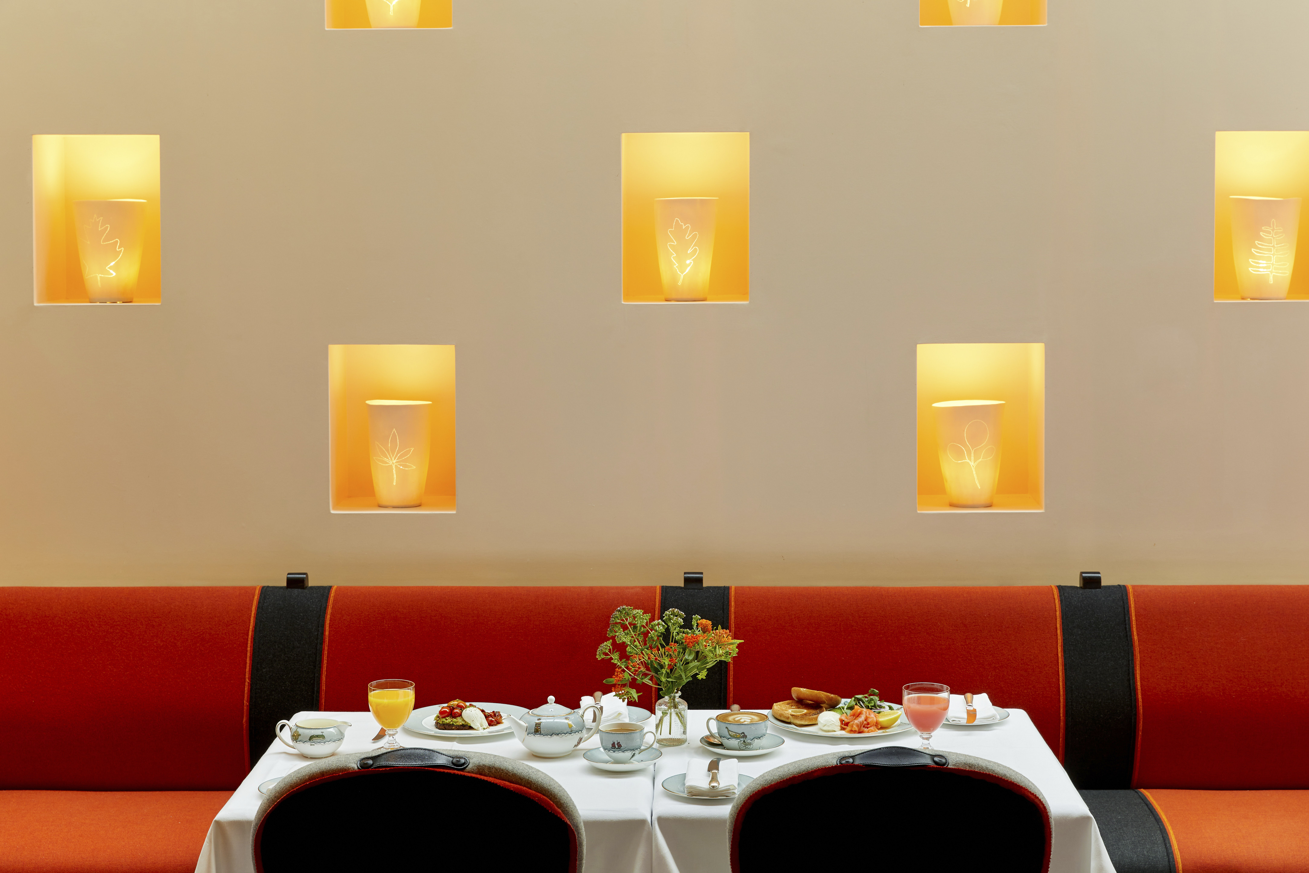 An image to promote breakfast at Ham Yard Hotel, The image shows a table filled with an array of breakfast dishes, including a smoked salmon bagel, avocado toast, and other colourful plates, alongside glasses of fresh juice.