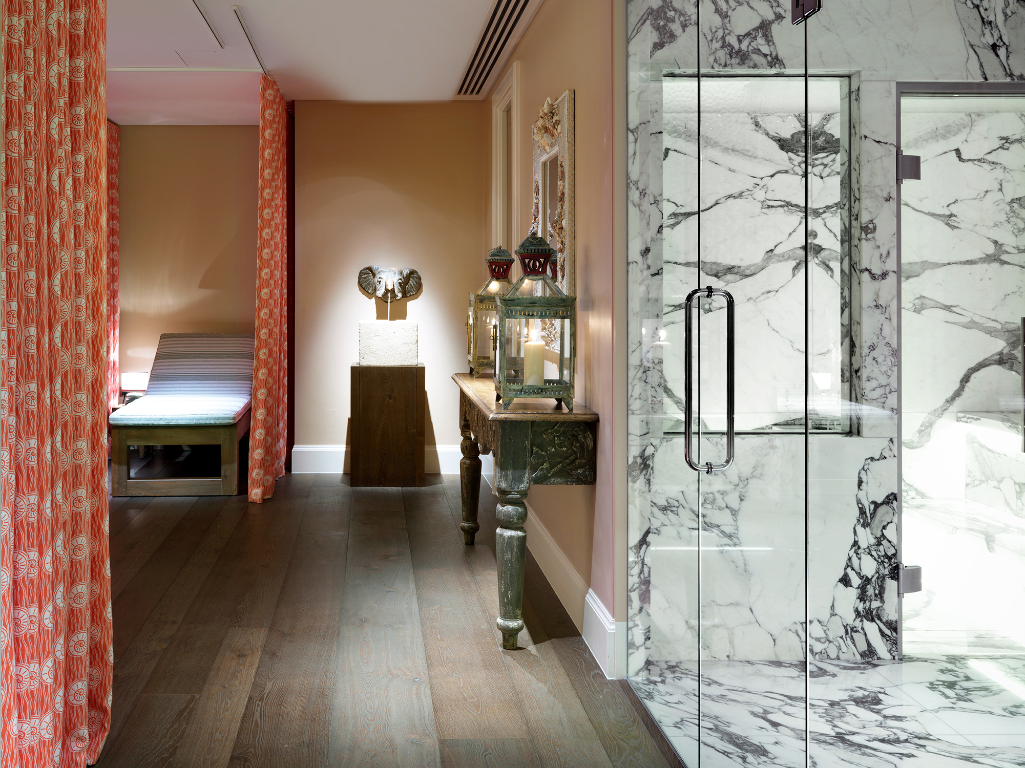 An image of the Soholistic Spa interior, on the left a relaxation lounger, an elephant sculpture on a pedestal, on the right a glass door leads into a white marble steam room.