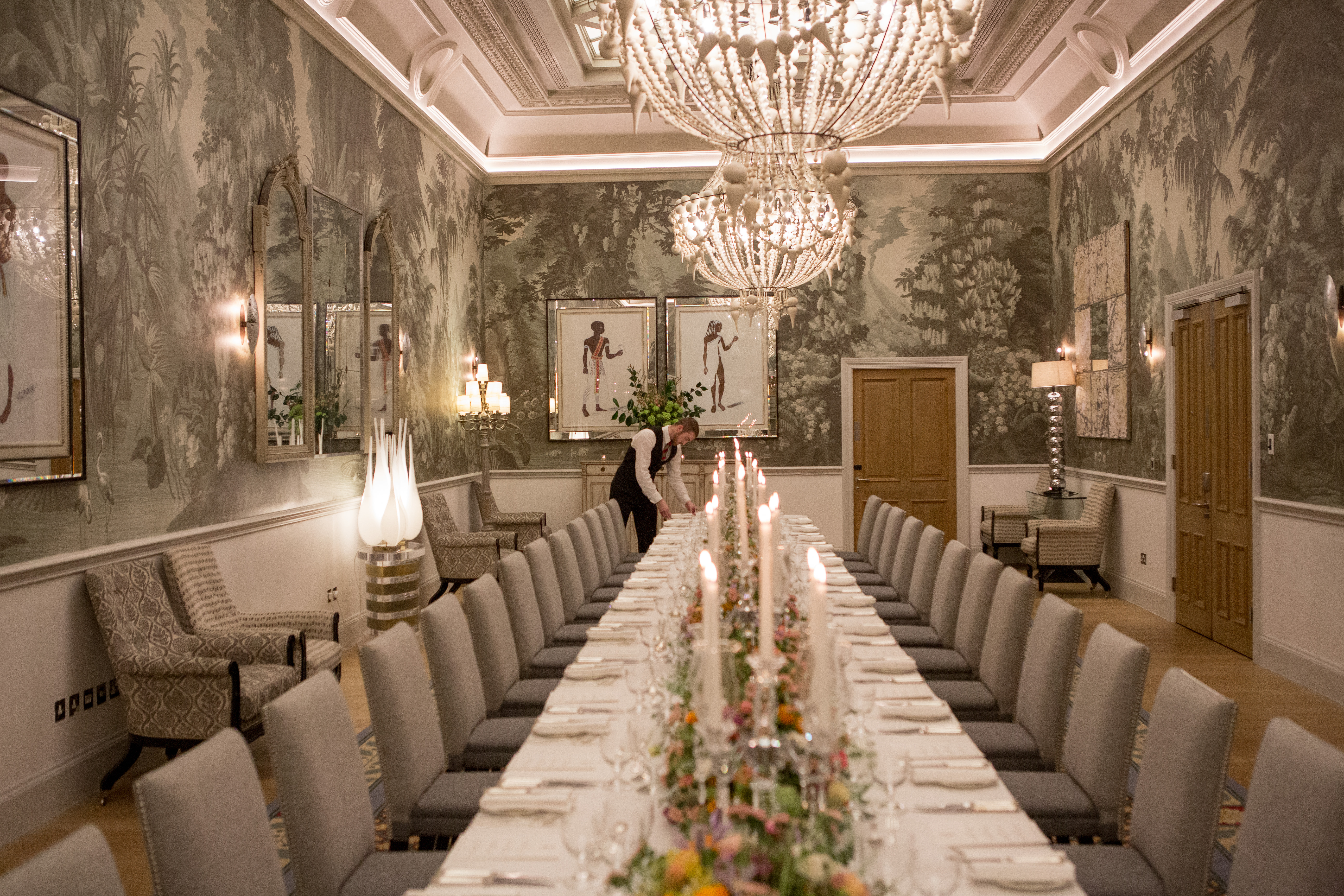 Wide shot of a long dining table dressed with colourful flowers and tall candlesticks in the Shooting Gallery private events room at Haymarket Hotel