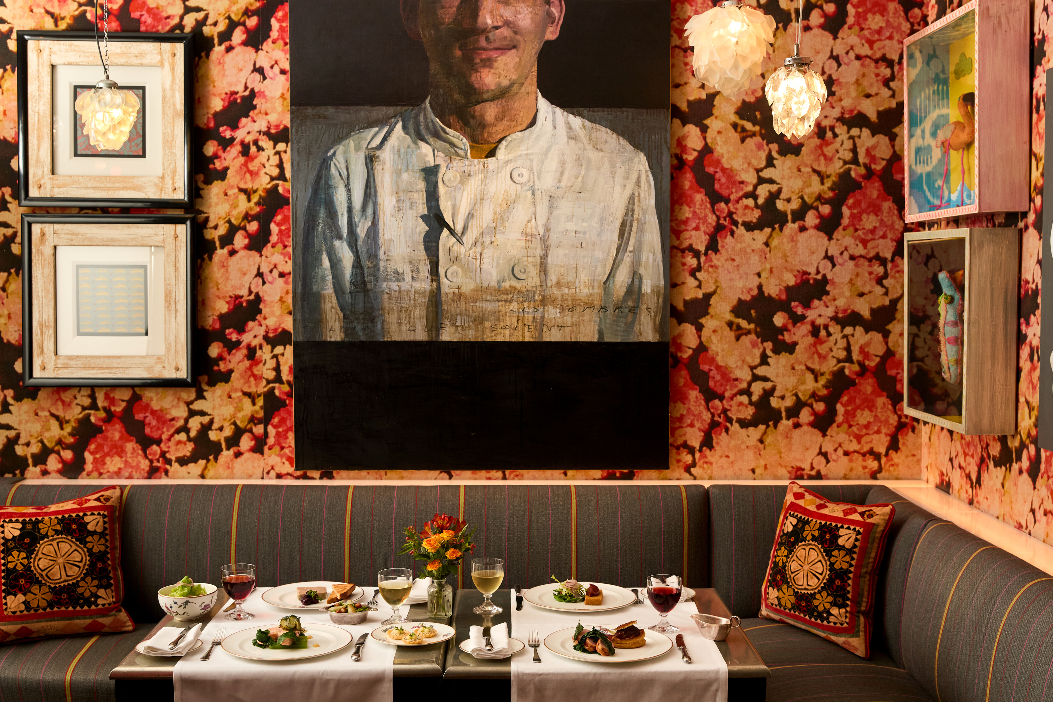 A image of a table at Refuel at Soho Hotel with white linen clothes is set up with multiple dishes from the Summer A La Carte with glasses of red and white wine on each place setting.