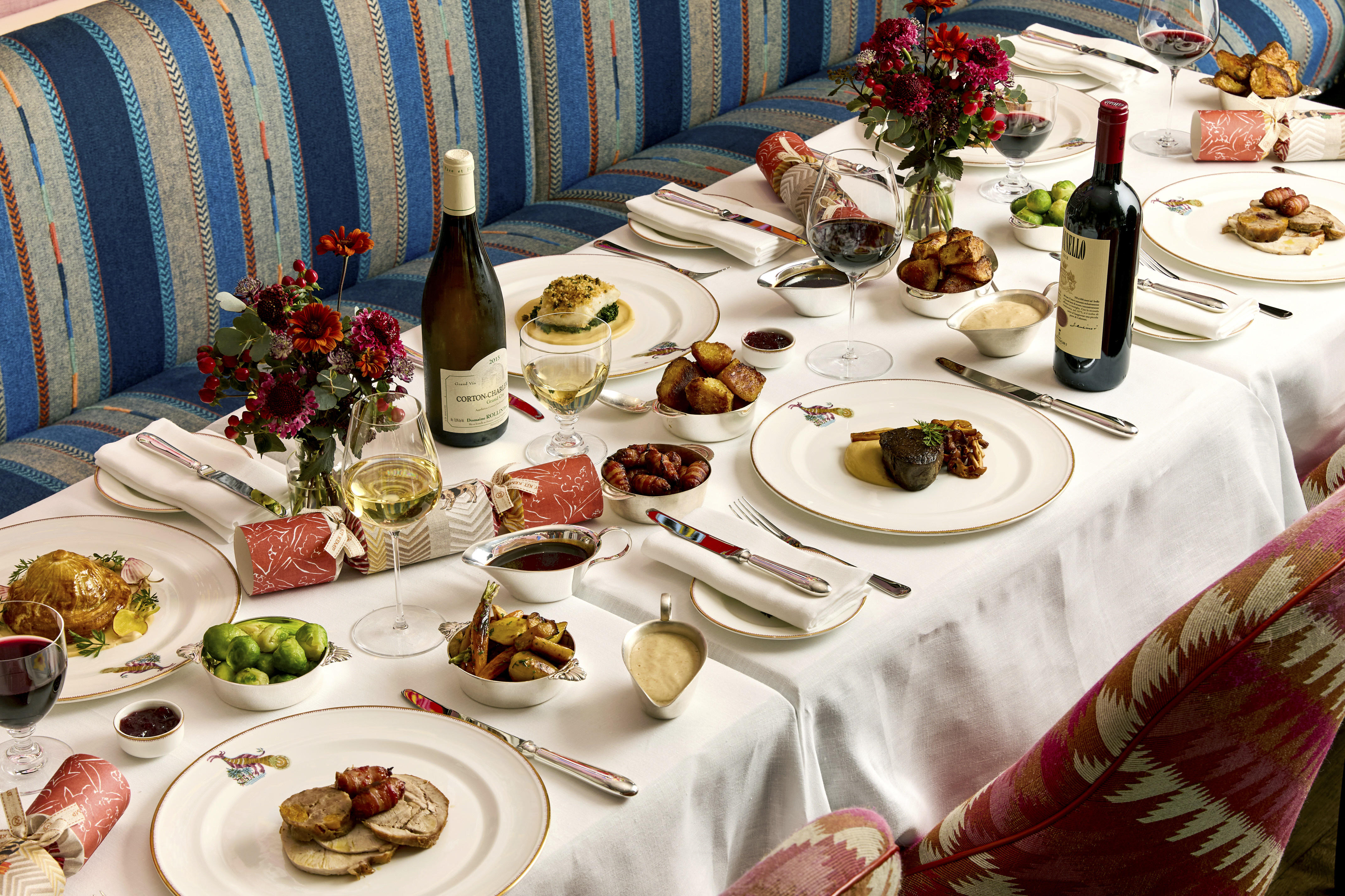 A table of six set up for Christmas dining at Brumus. There are plates of meat and fish with small side dishes and bottles of wine