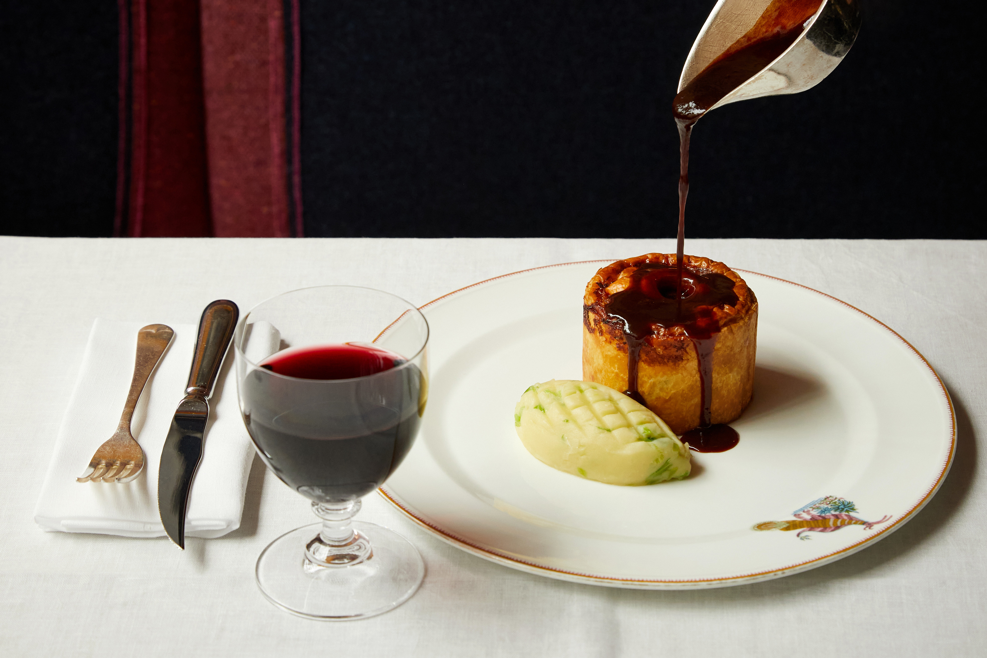 Gravy is poured over a main course of pie and mash on a plate with a glass of wine at Brumus