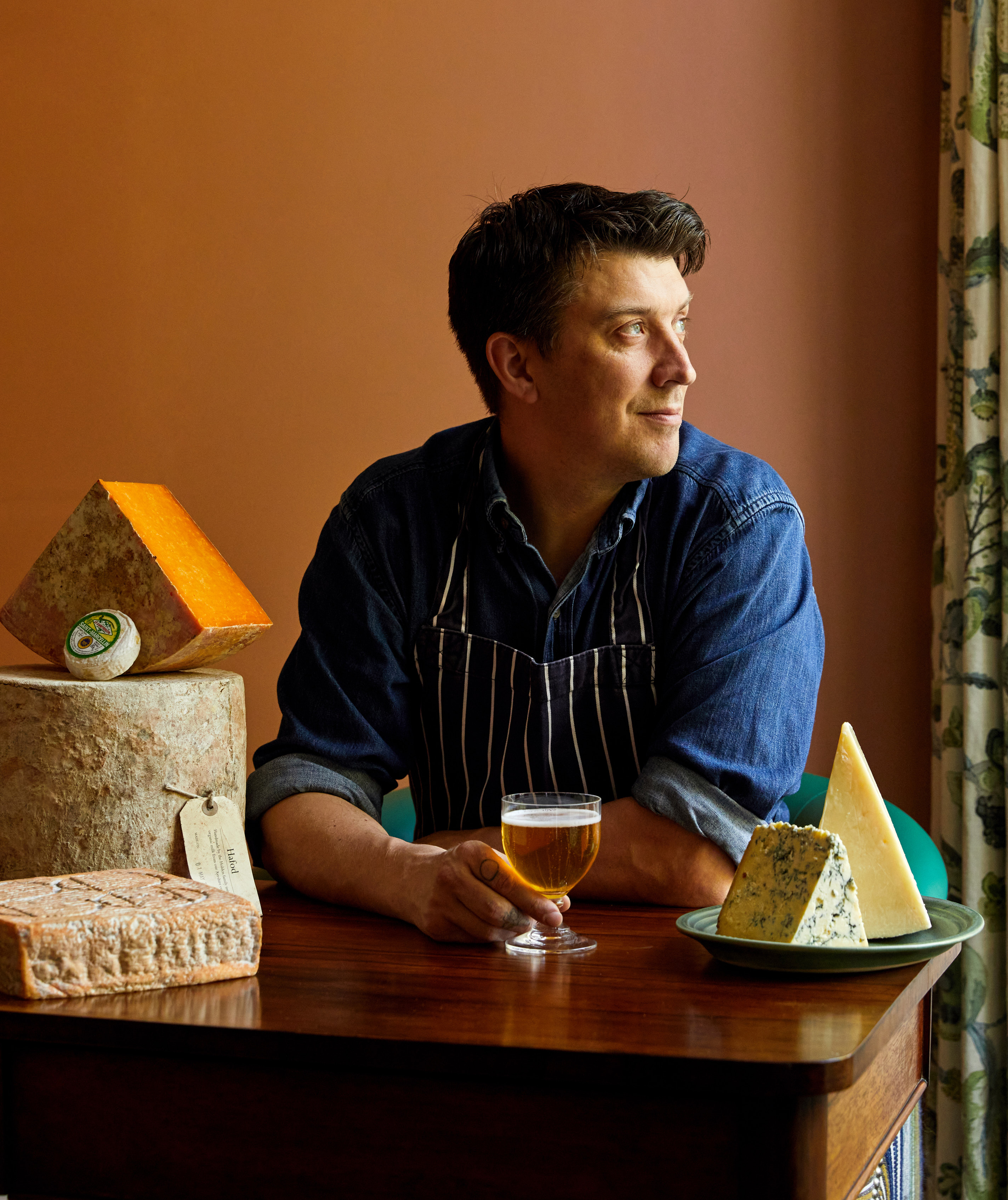 An image of Joe Fox holding a glass of beer surrounded by different cheeses at The Potting Shed, Dorset Square Hotel.
