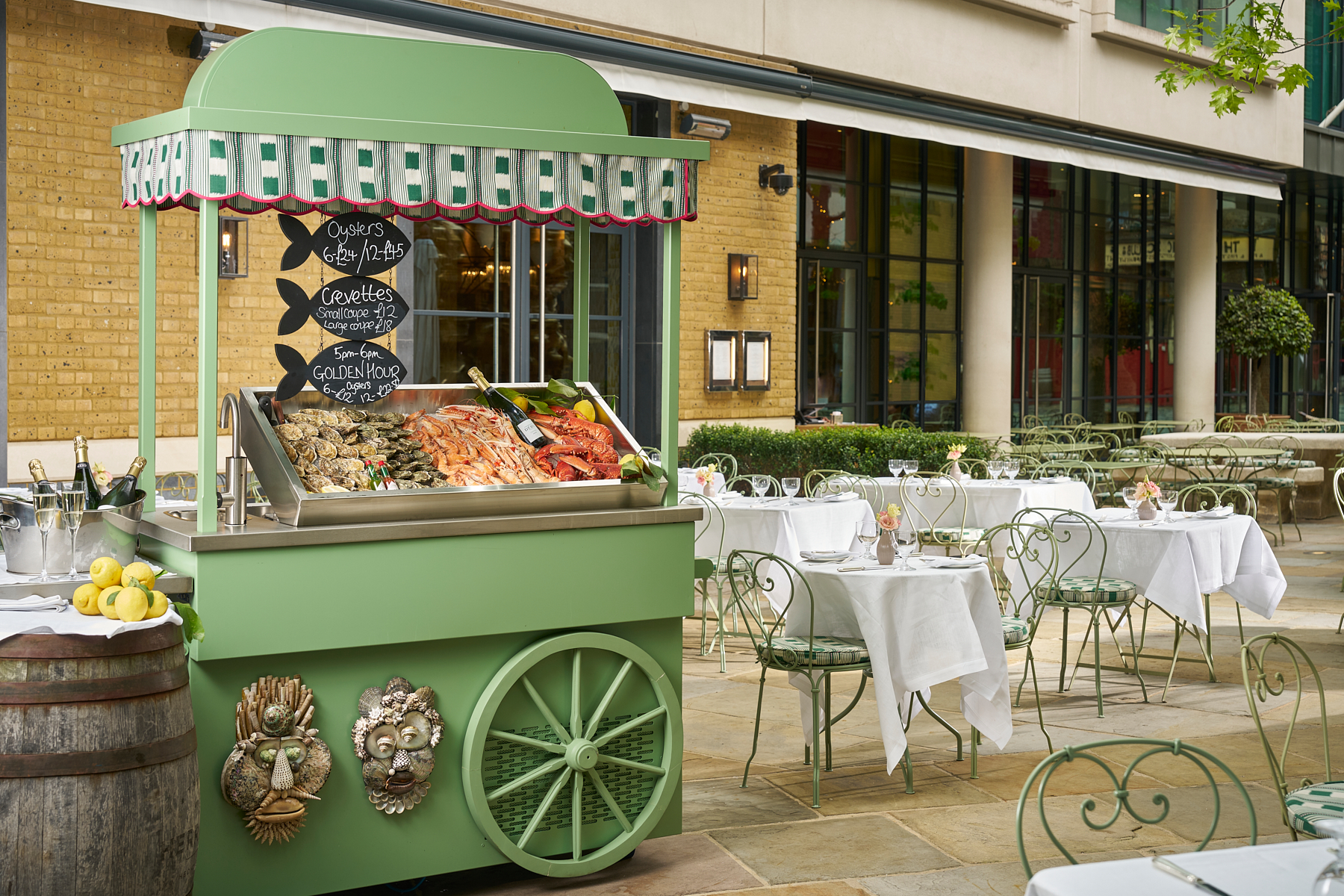 Wide shot of the exterior of Ham Yard Hotel featuring a green oyster cart and tables set up for outdoor dining