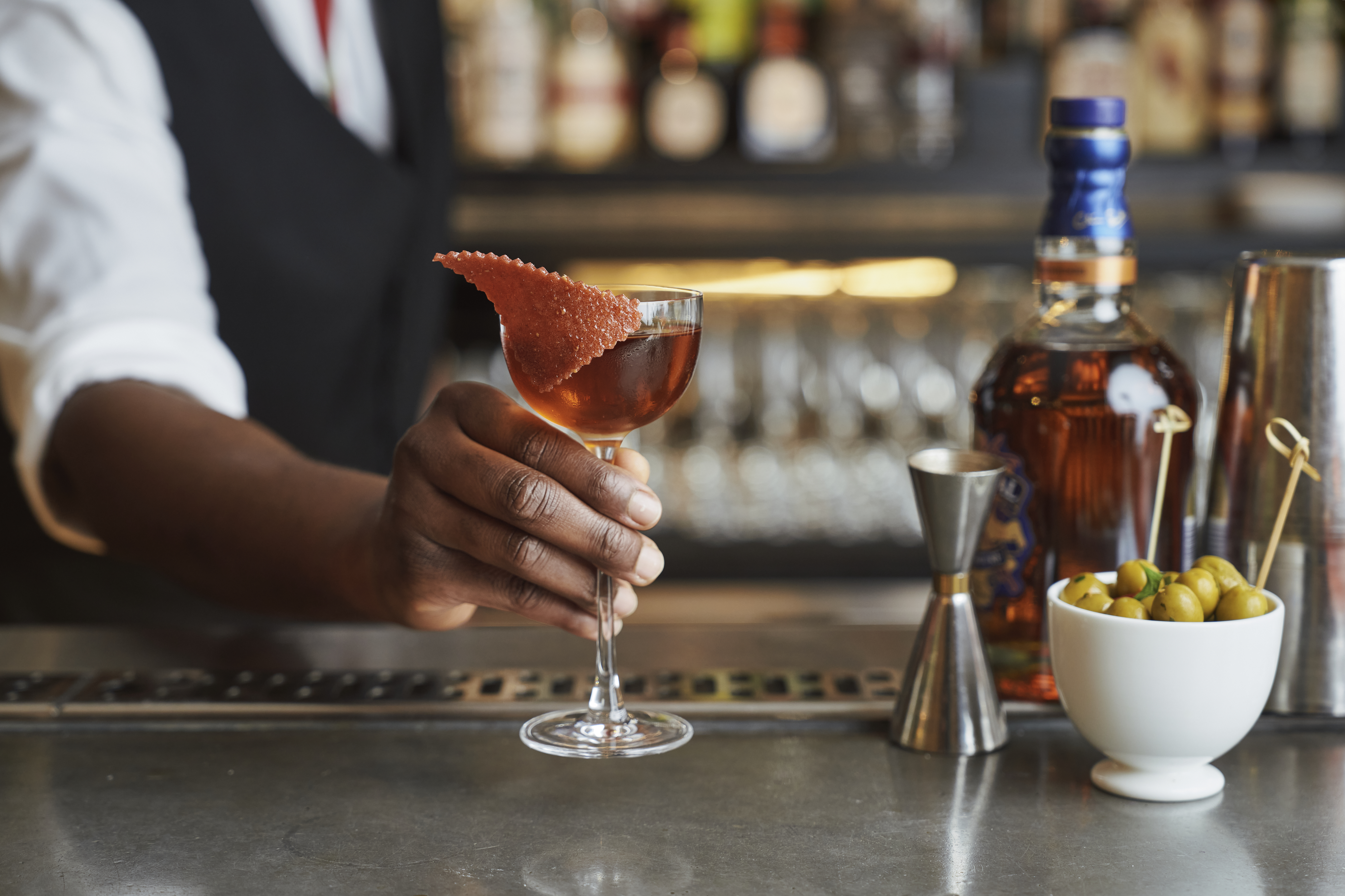 Wide shot of a bartender presenting a cocktail on the bar at Ham Yard