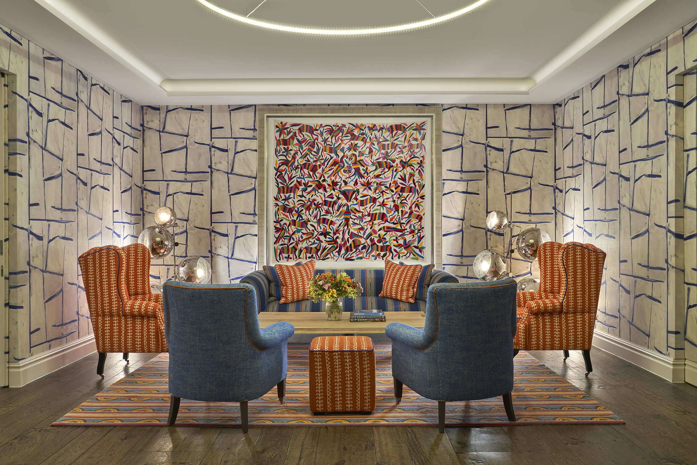 An image of the seating area in the Sandra Blow private events room at The Soho Hotel. The image shows a sofa in a blue and orange colour scheme under a piece of art, with two orange armchairs flanking the sofa and two blue arm chairs at the front facing away from the camera.