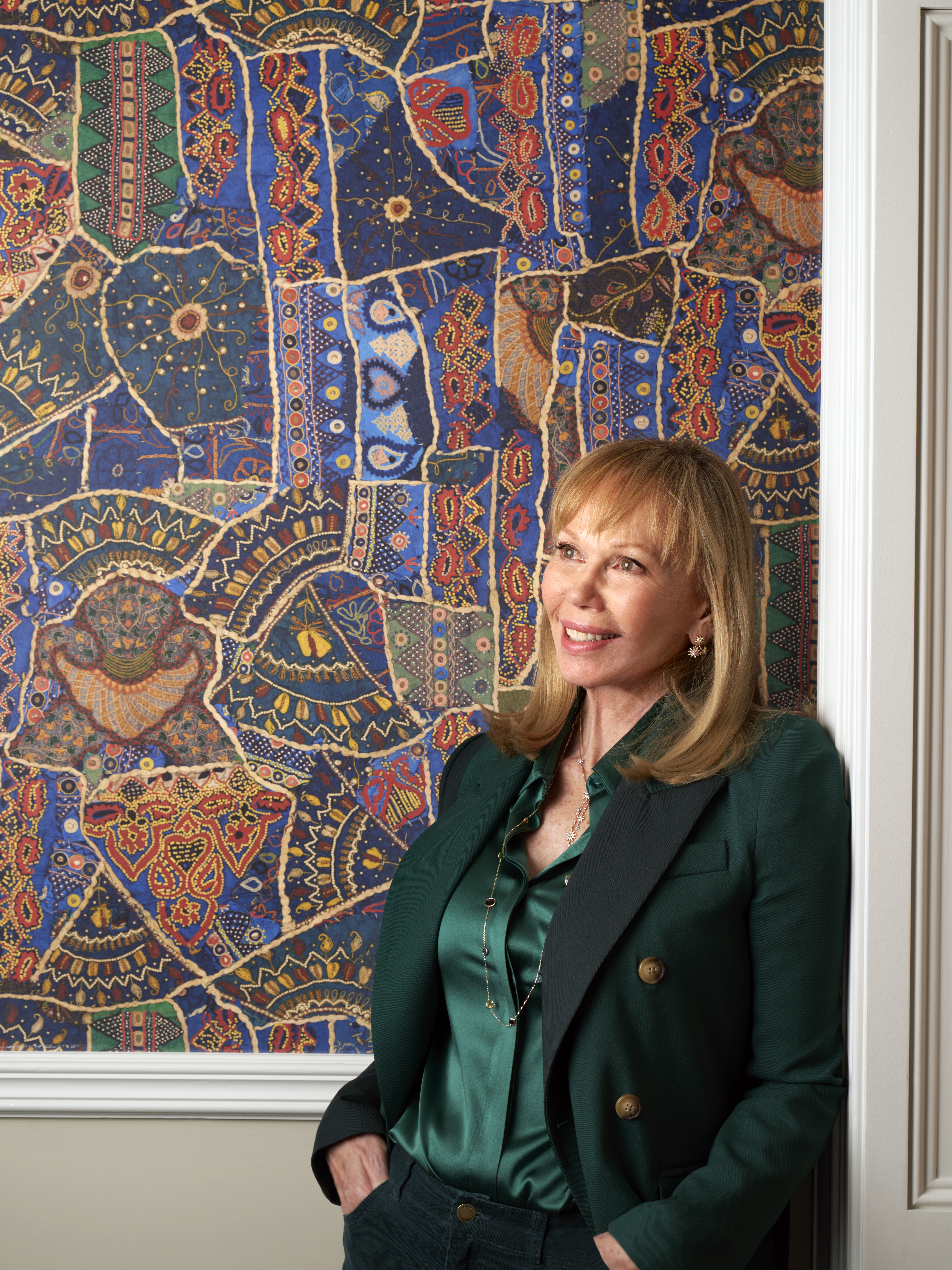 A portrait image of Kit Kemp in front of a wall covered in Kit Kemp x GP & J Baker's Front Row in Jewel Blue. In the image she is leaning against the wall looking to the left.
