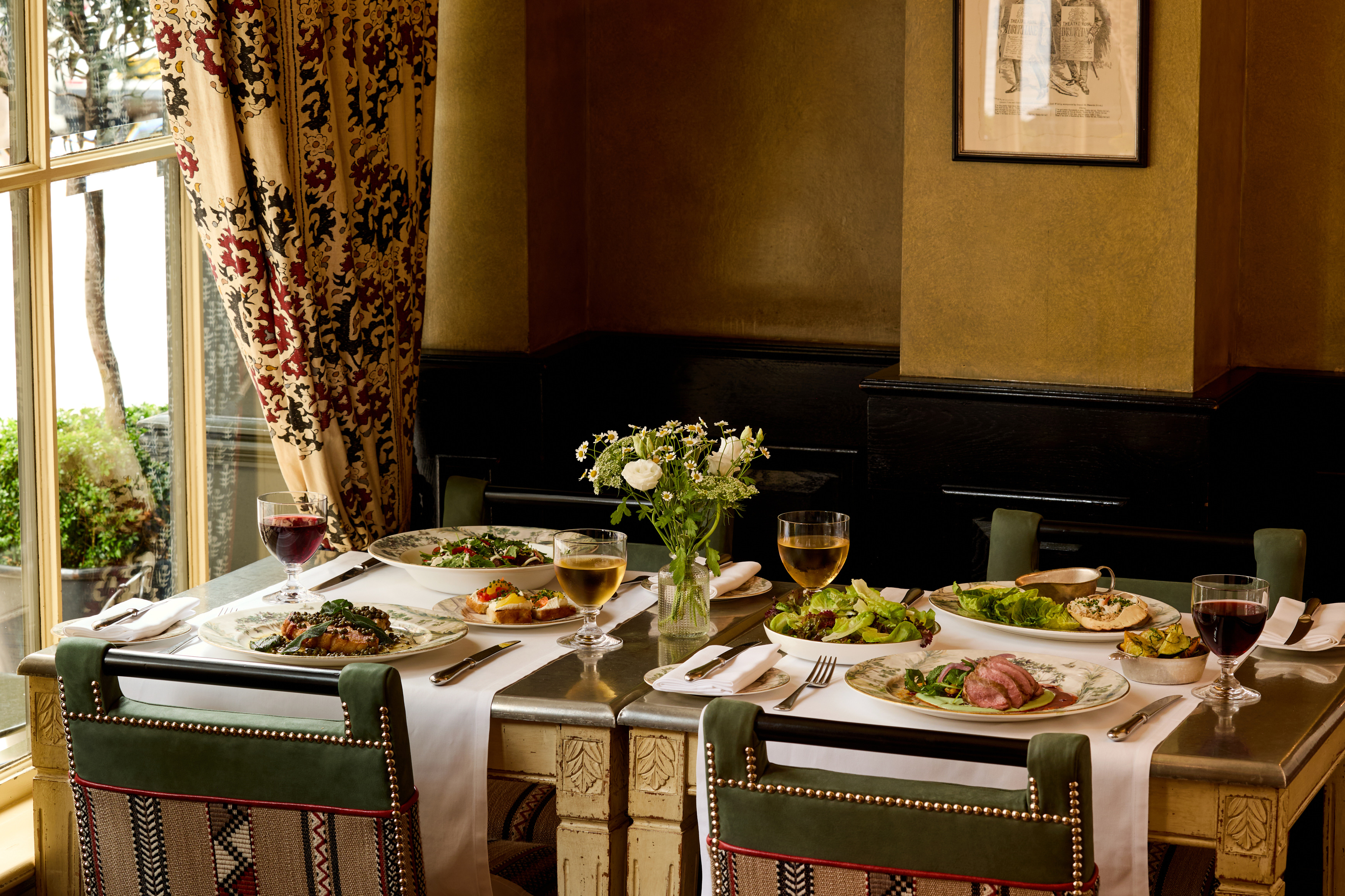 An image to promote Brasserie Max’s À La Carte menu at Covent Garden Hotel. The image shows a variety of dishes on the rectangular table and glasses of wine.