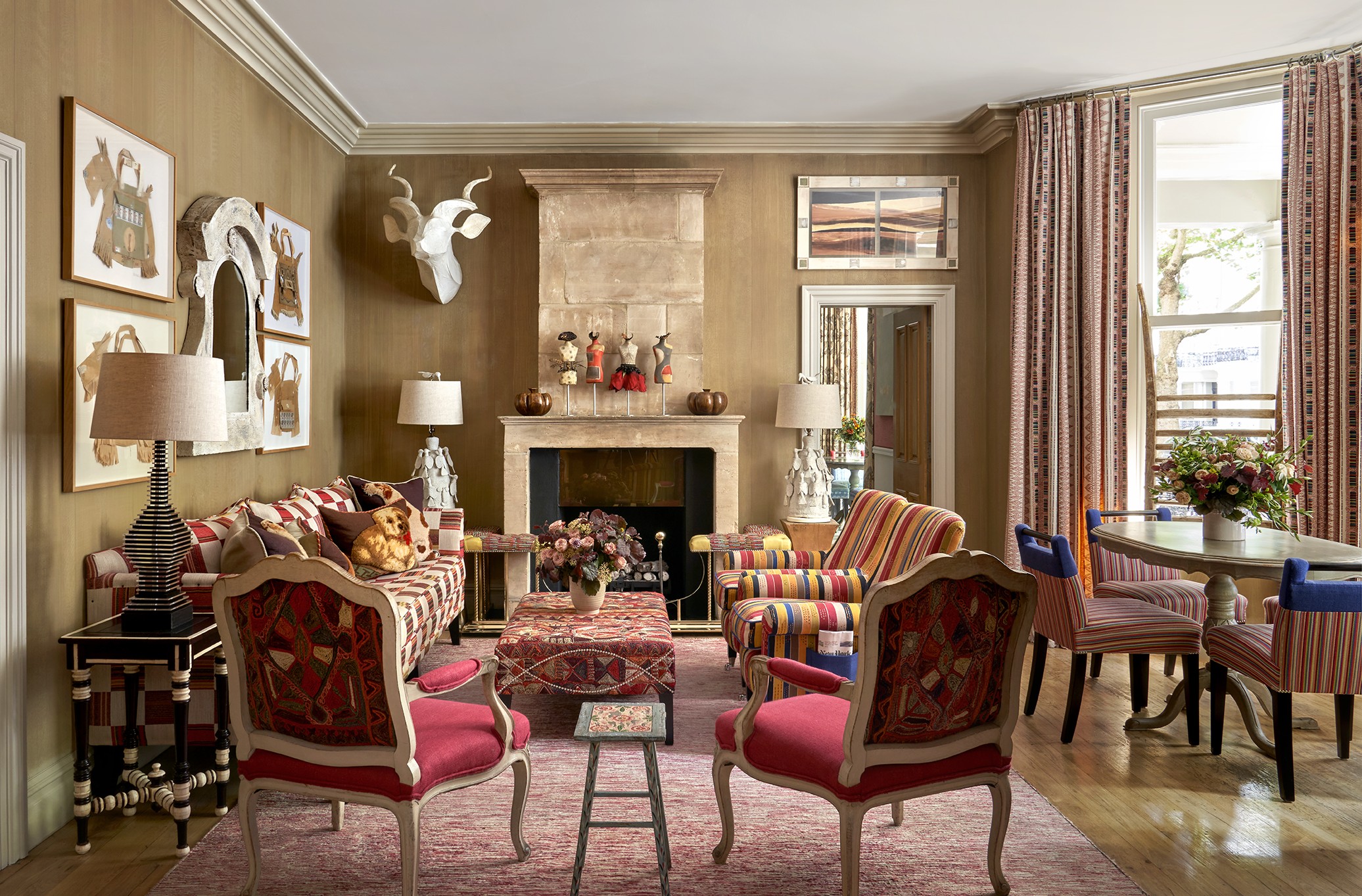 Wide shot of the Drawing Room at Knightsbridge Hotel, the room displays a sofa on the left, in the foreground the backs of two arm chairs that face into the room. in the centre a low embroidered coffee table, on the right hand side of the seating area, two striped arm chairs. On the fart right of the image we see a round dining table with 4 striped chairs around it.
