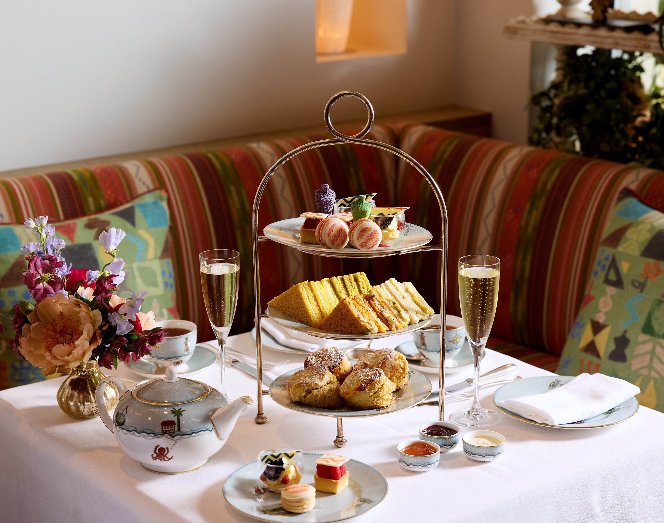 The Kit Kemp Design Thread Afternoon Tea set up at The Whitby Bar. There is a cake stand with scones, cakes decorated with Kit Kemps Famous fabrics, edible mannequins and sandwiches with tea and Champagne