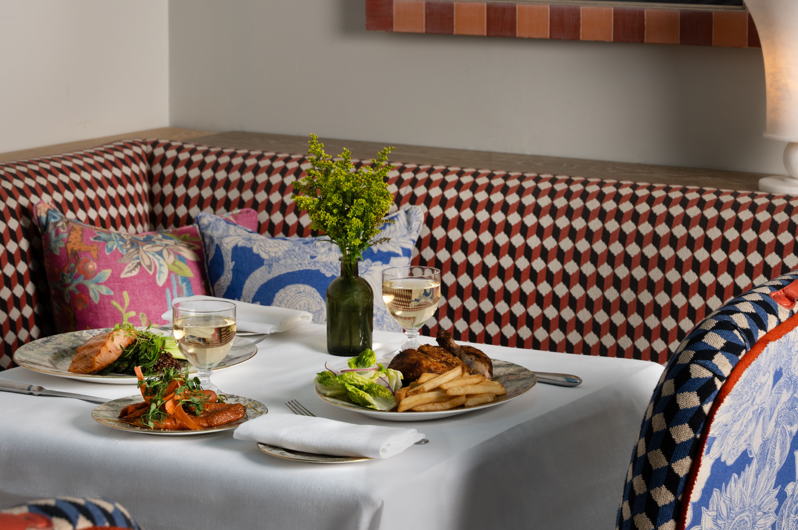 A wide angle shot of a table set up for dinner in Warren Street Bar. There are dishes of Lancaster chicken and grilled salmon, with white wine pairings