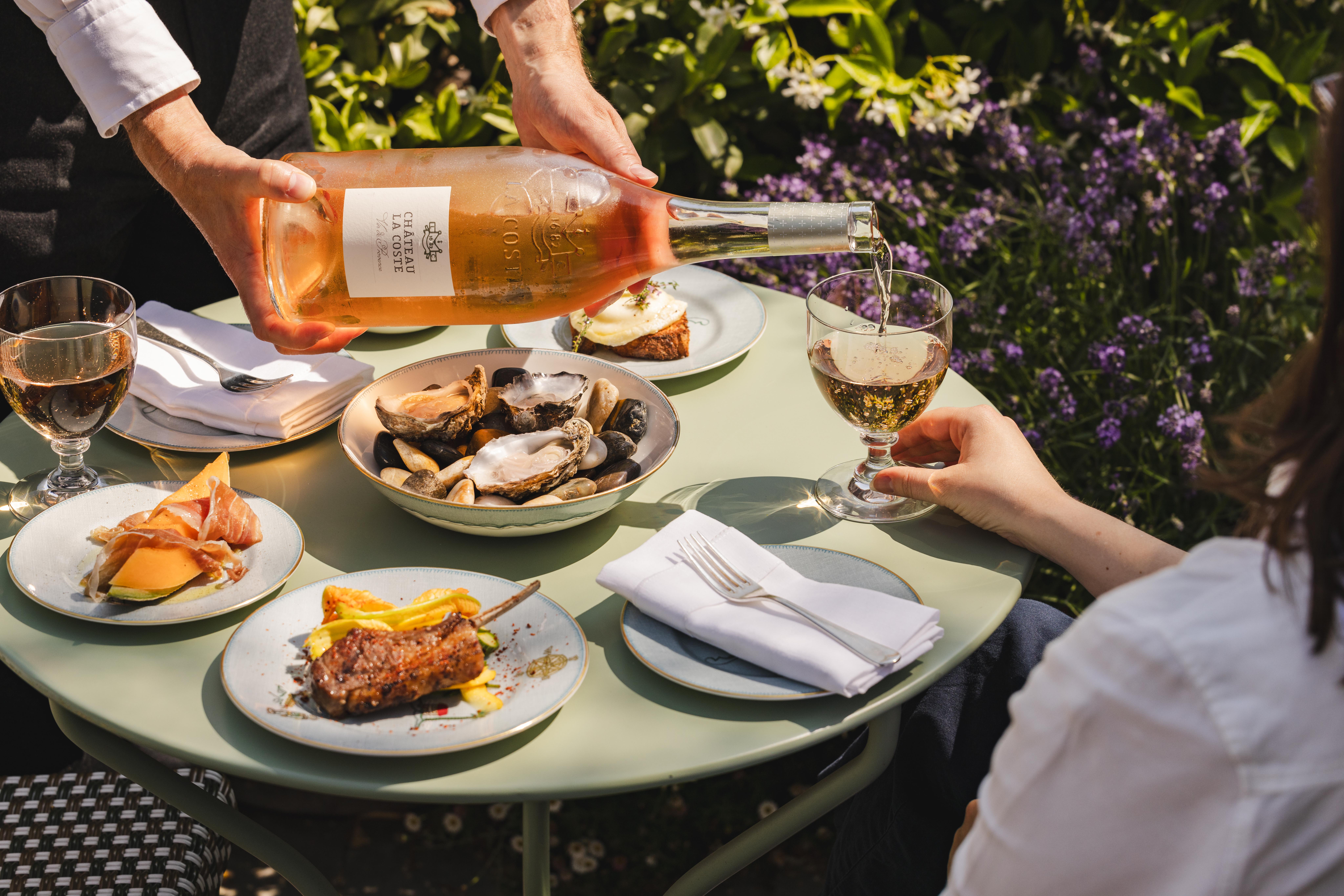 An image of a waiter pouring a bottle Chateau Le Coste with some dishes from the 'Rose on the Roof' menu at Ham Yard Hotel.