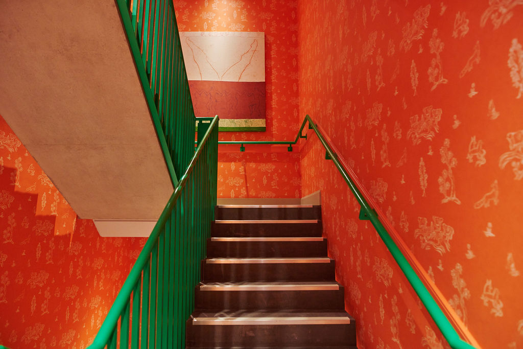 A wide shot of the colourful stairwell. The walls have been lined in Kit Kemp's Friendly Folk and the hand rail has been painted in a bright emerald green at 9-11 Richmond Buildings.