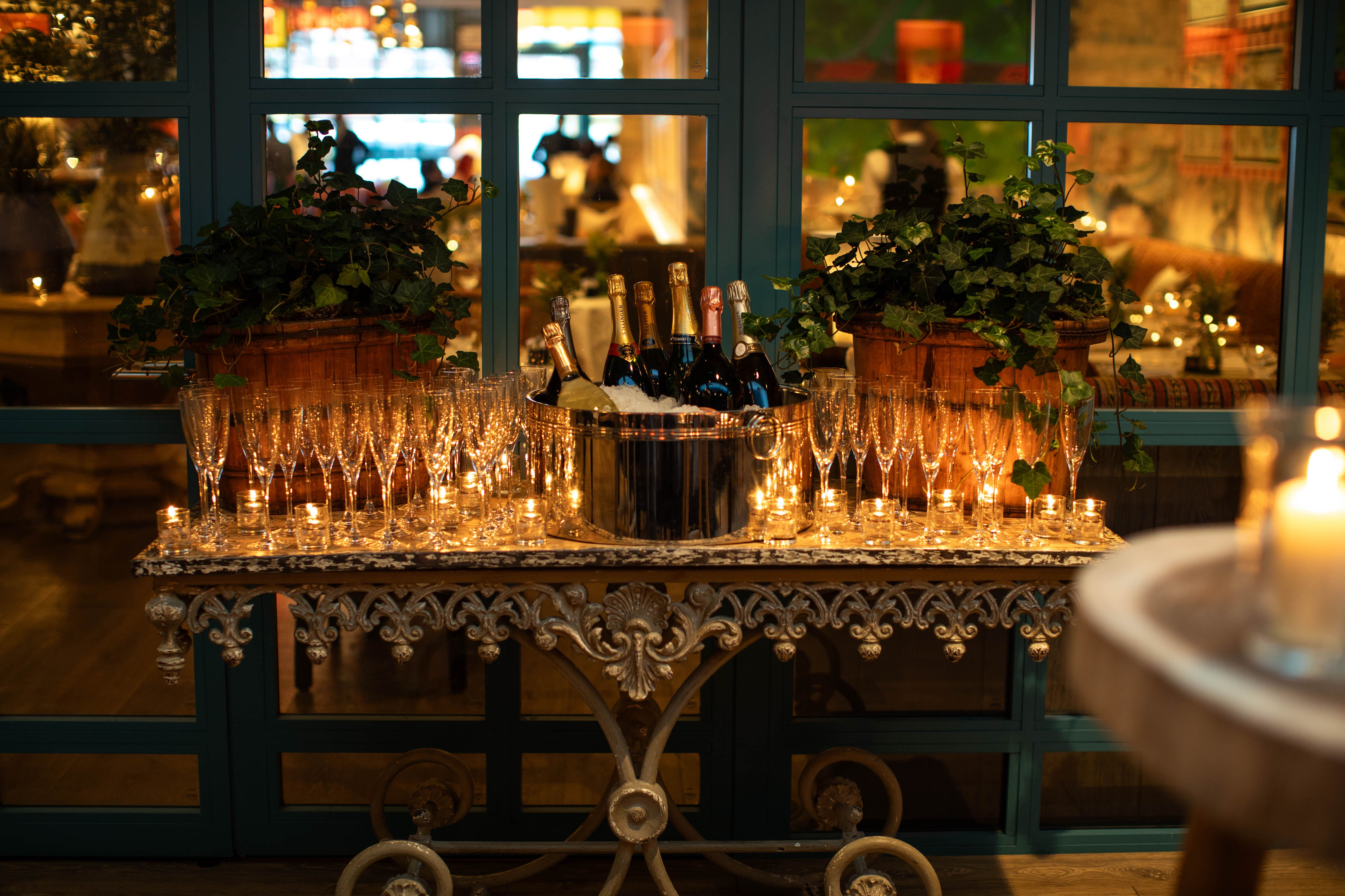 A table laid with Champagne glasses and tealights. In the middle there is an ice bucket full of bottles of Champagne