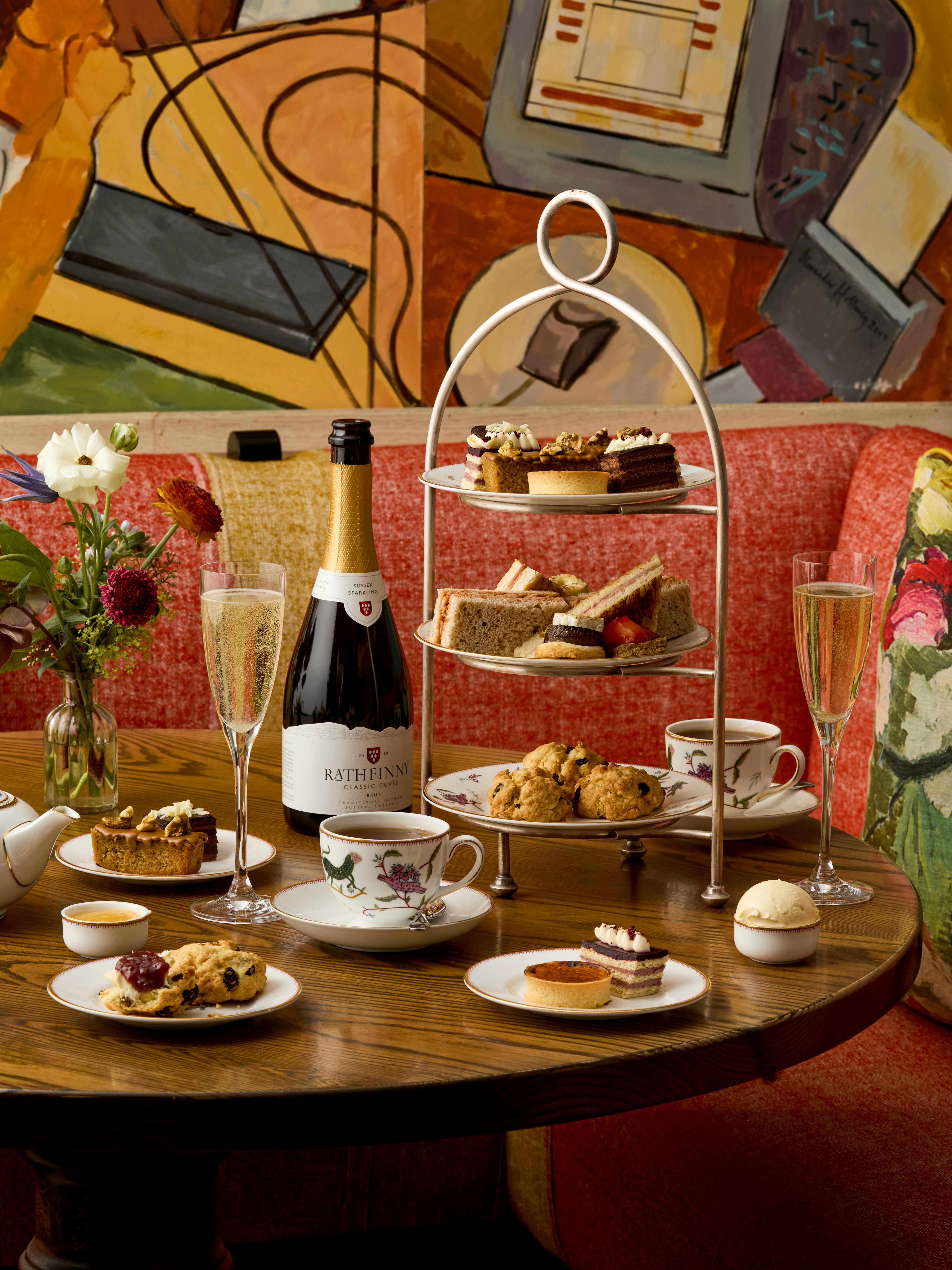 A portrait shot of the Bloomsbury Set Afternoon Tea at Oscar: There is one afternoon tea stand on the table next to a bottle of sparkling wine