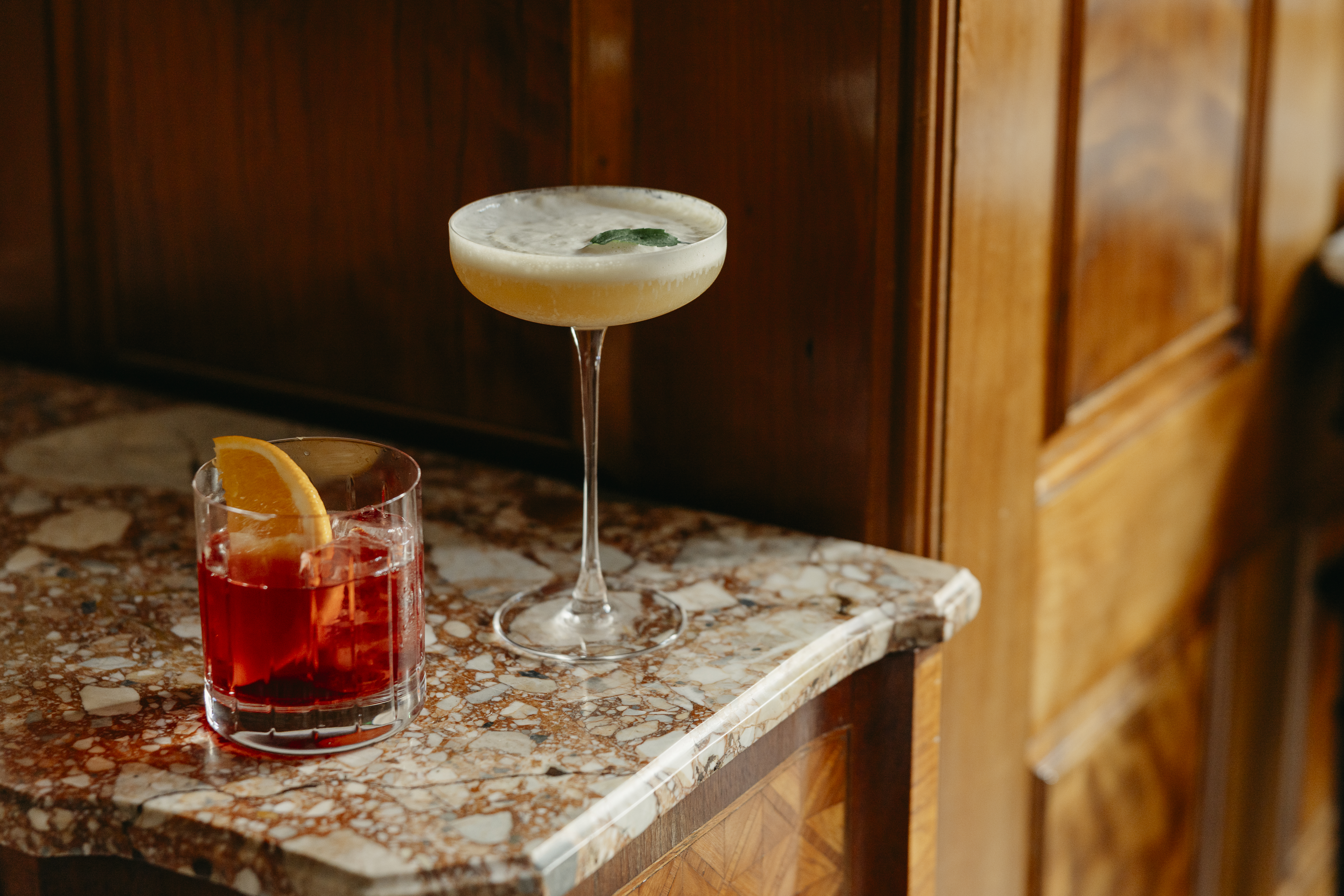 A close up short of a negroni and martini cocktail on a marble surface in Brasserie Max