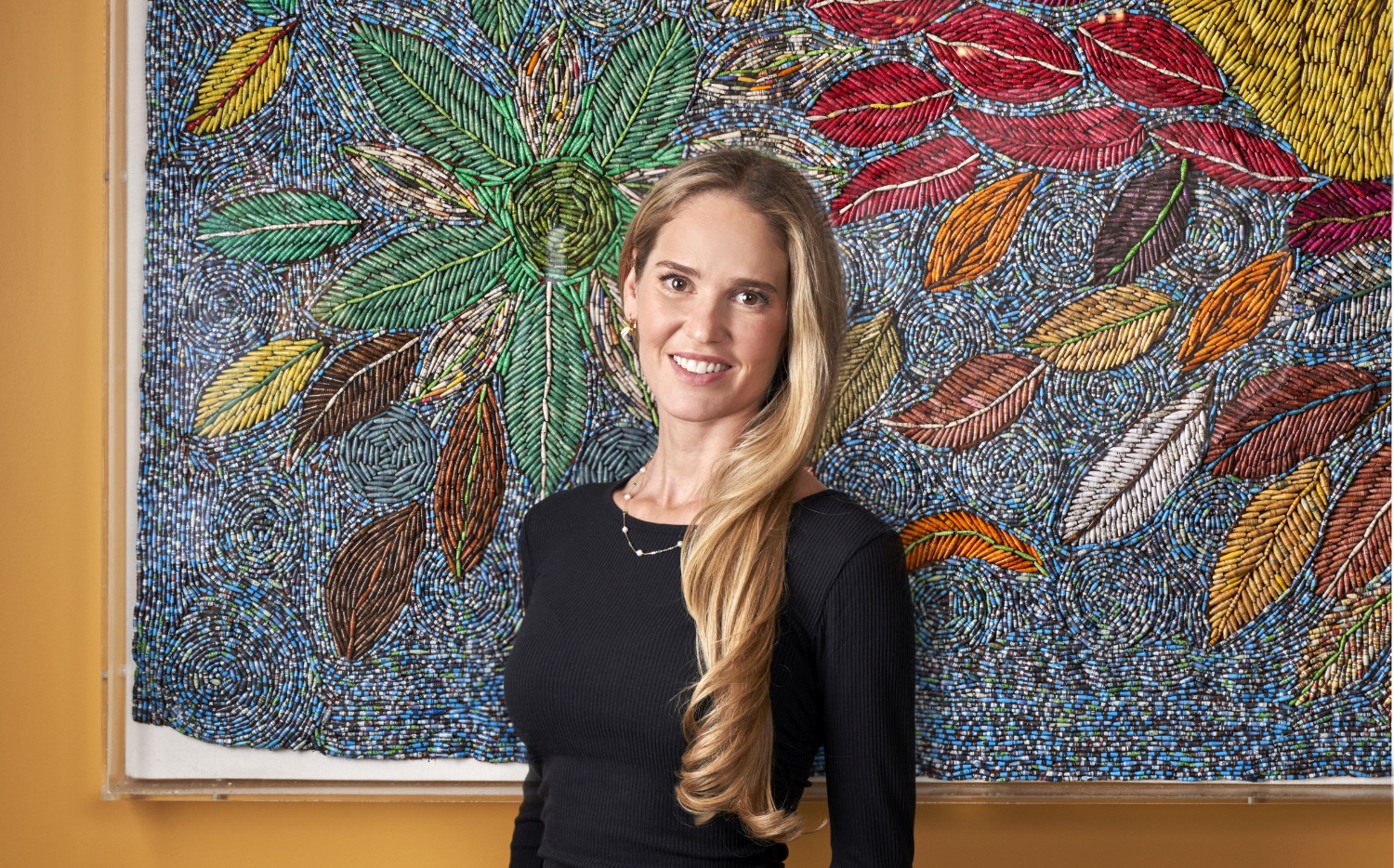Willow Kemp stands in front of a piece of art work made up of small paper beads