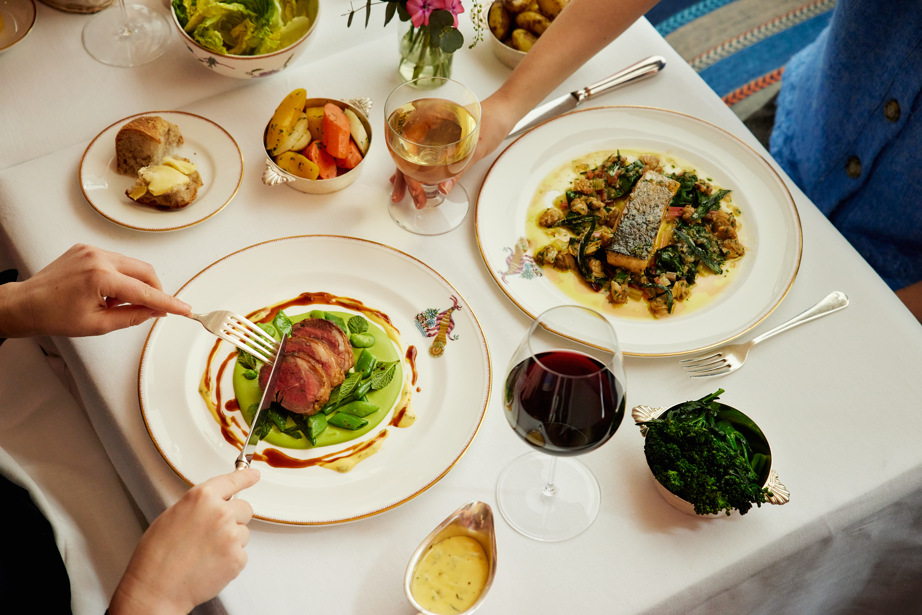 A wide angle shot of two people enjoying dinner at Brumus: there is a selection of dishes from the Summer A La Carte menu, along with wine pairings