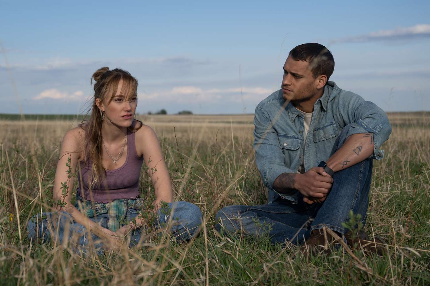 A still from the film "Reminders of Him" showing a man and a woman sitting in a field.