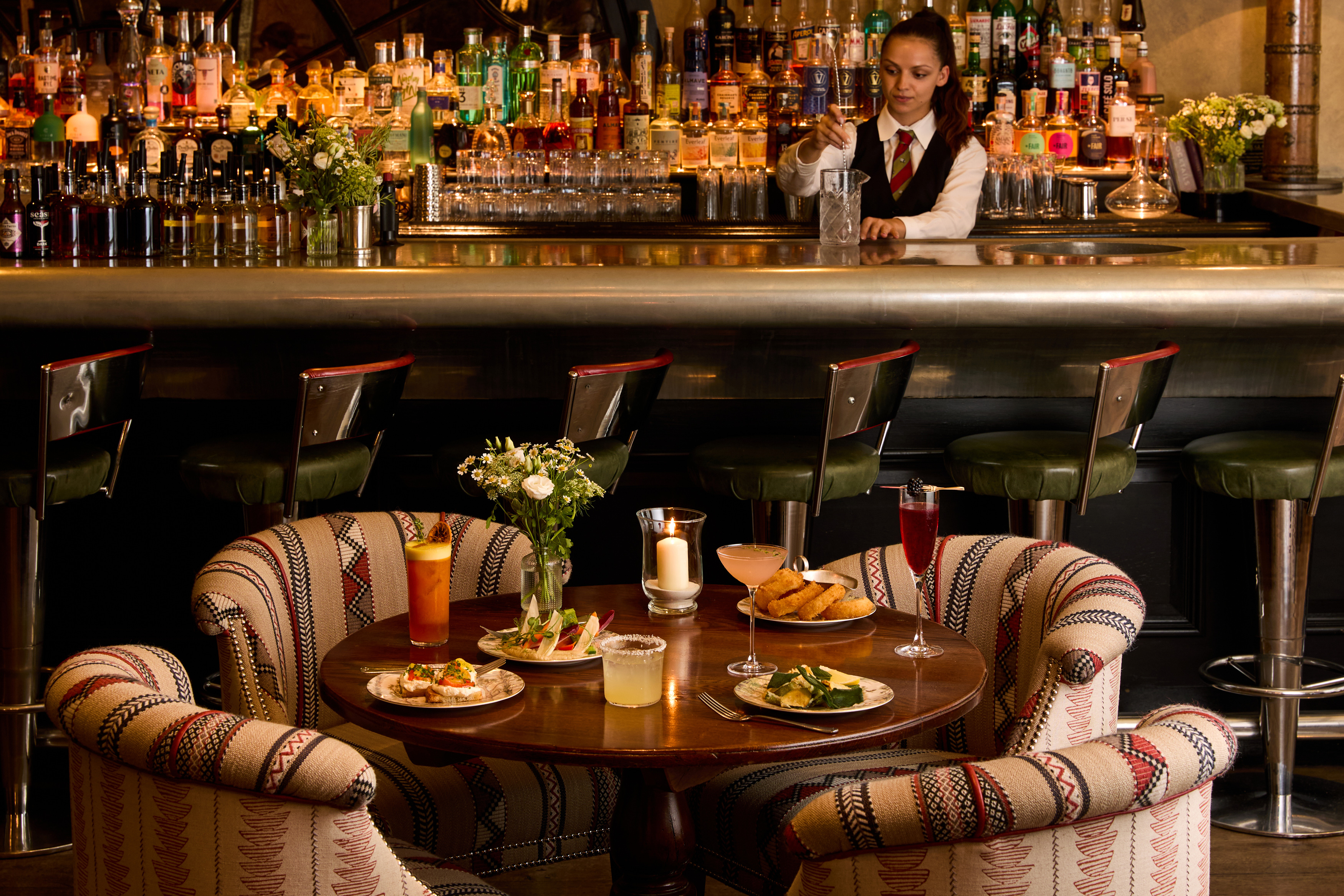 An image to promote Brasserie Max’s À La Carte menu at Covent Garden Hotel. The image shows a variety of dishes on the round table and a selection of cocktails.