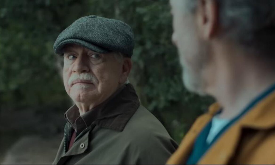 A still from the film "Glenrothan": Two men stand outside facing one another, the focus being an elderly man wearing a flat cap