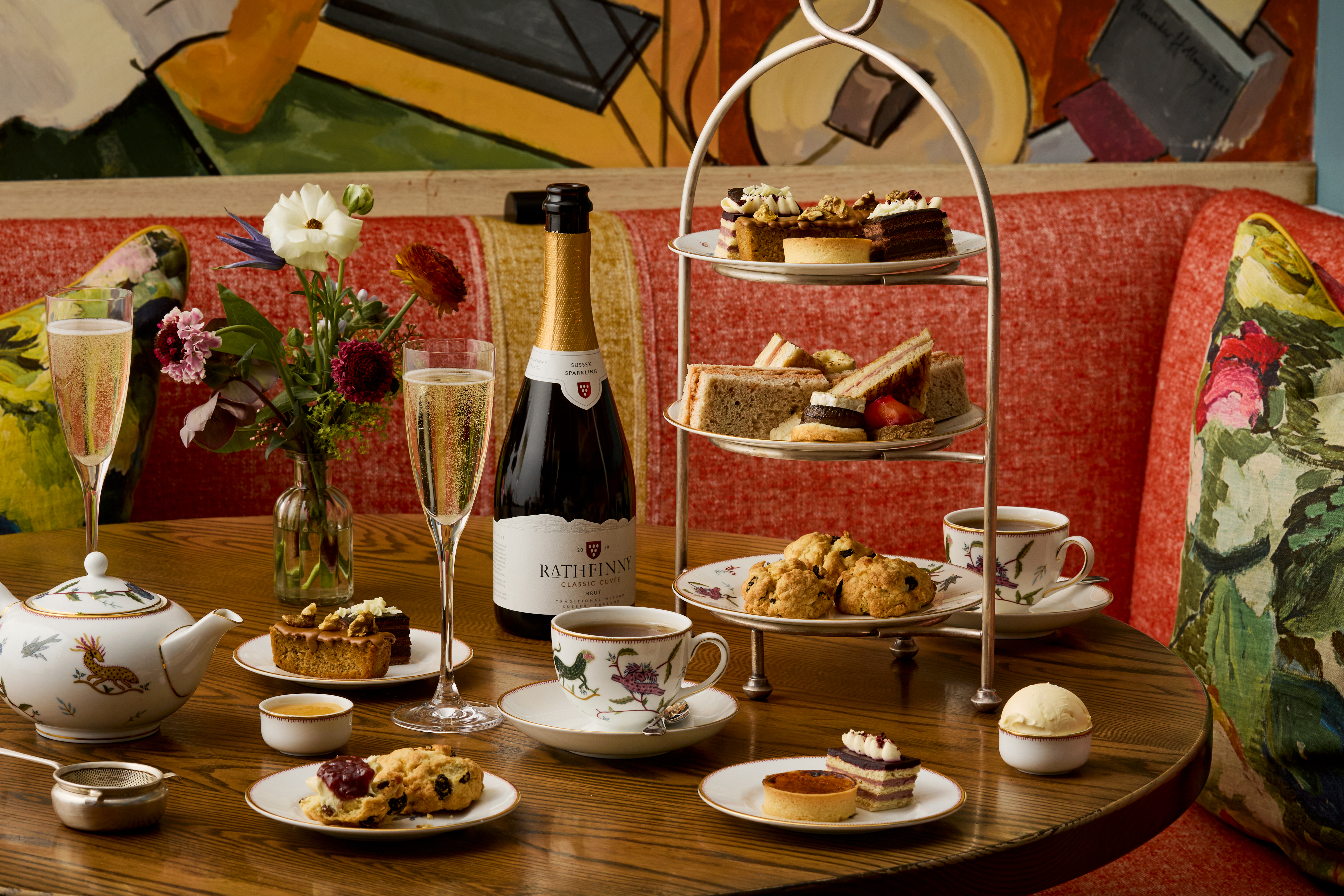 A wide shot of the Bloomsbury Set Afternoon Tea at Oscar: There is one afternoon tea stand on the table next to a bottle of sparkling wine