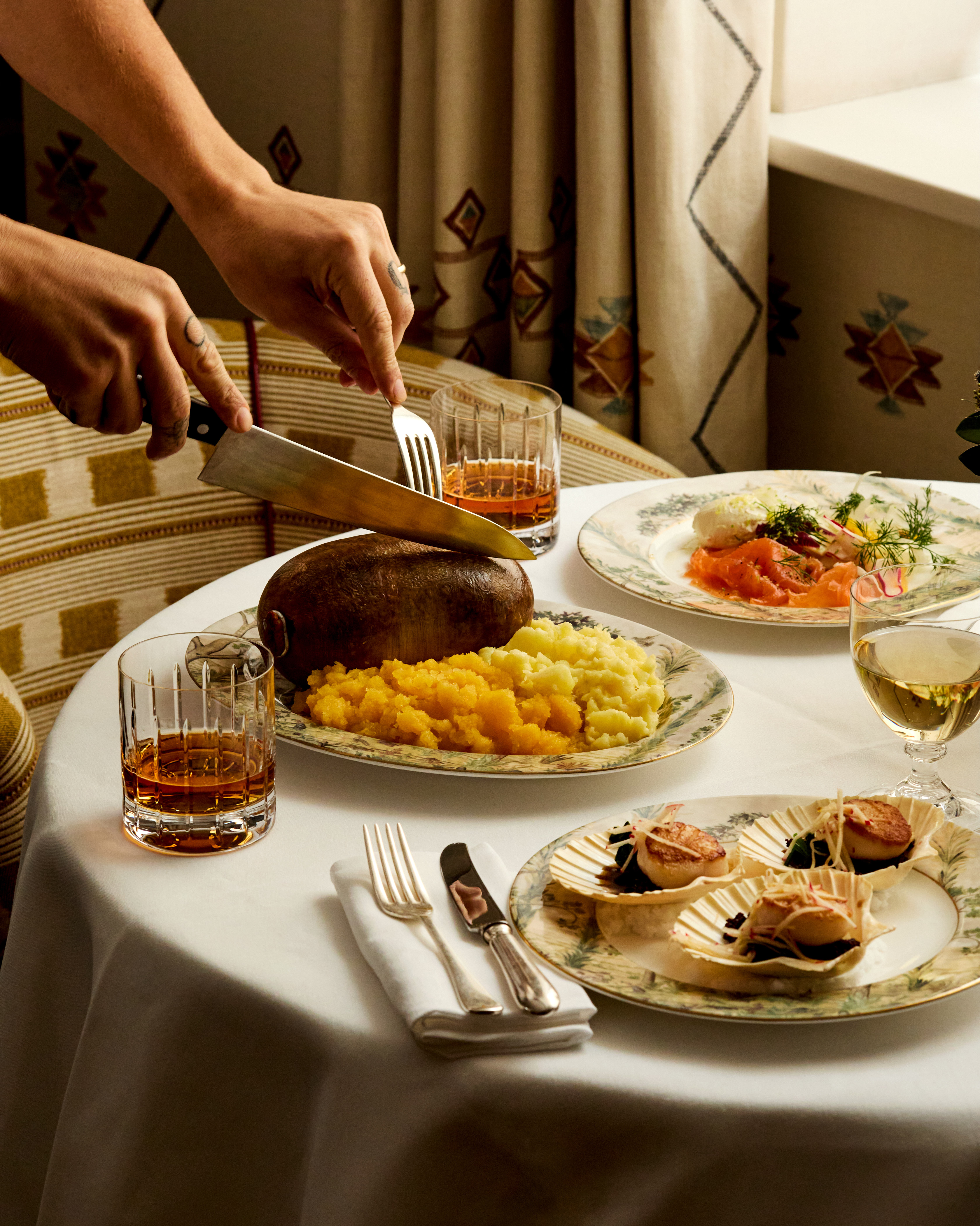 Portrait shot of a table set for Burns Night dinner with Bruichladdich at Covent Garden Hotel. There is a plate of haggis being cut open, plates of scallops and smoked salmon and glasses of whisky.