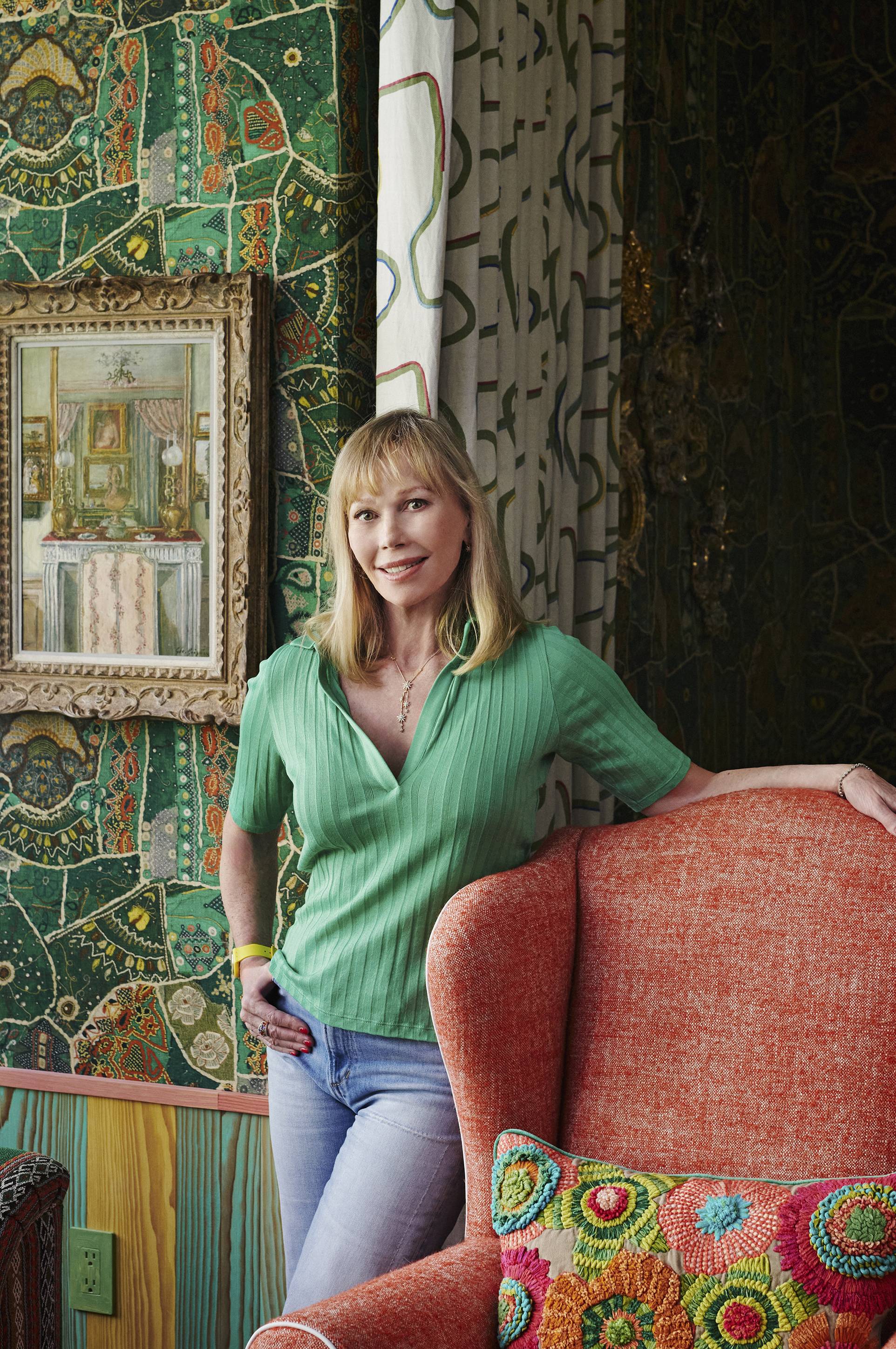 Firmdale Hotels Creative Director Kit Kemp standing her showroom at Kips Bay in New York. She stands in front of a patterned wall leaning on a red armchair