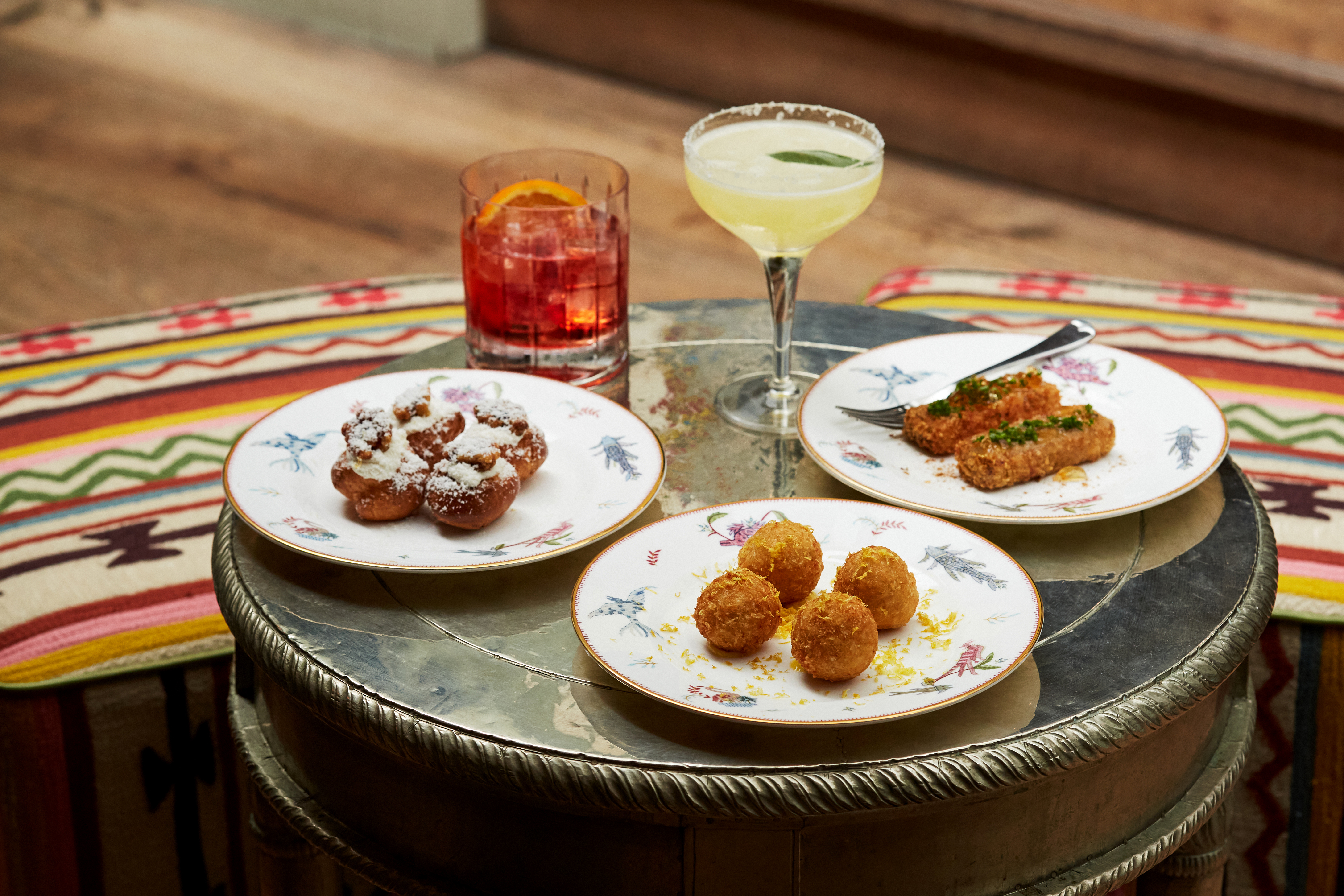 Wide shot of bar food on a table at The Potting Shed. Plates of arancini and croquettes with two cocktails